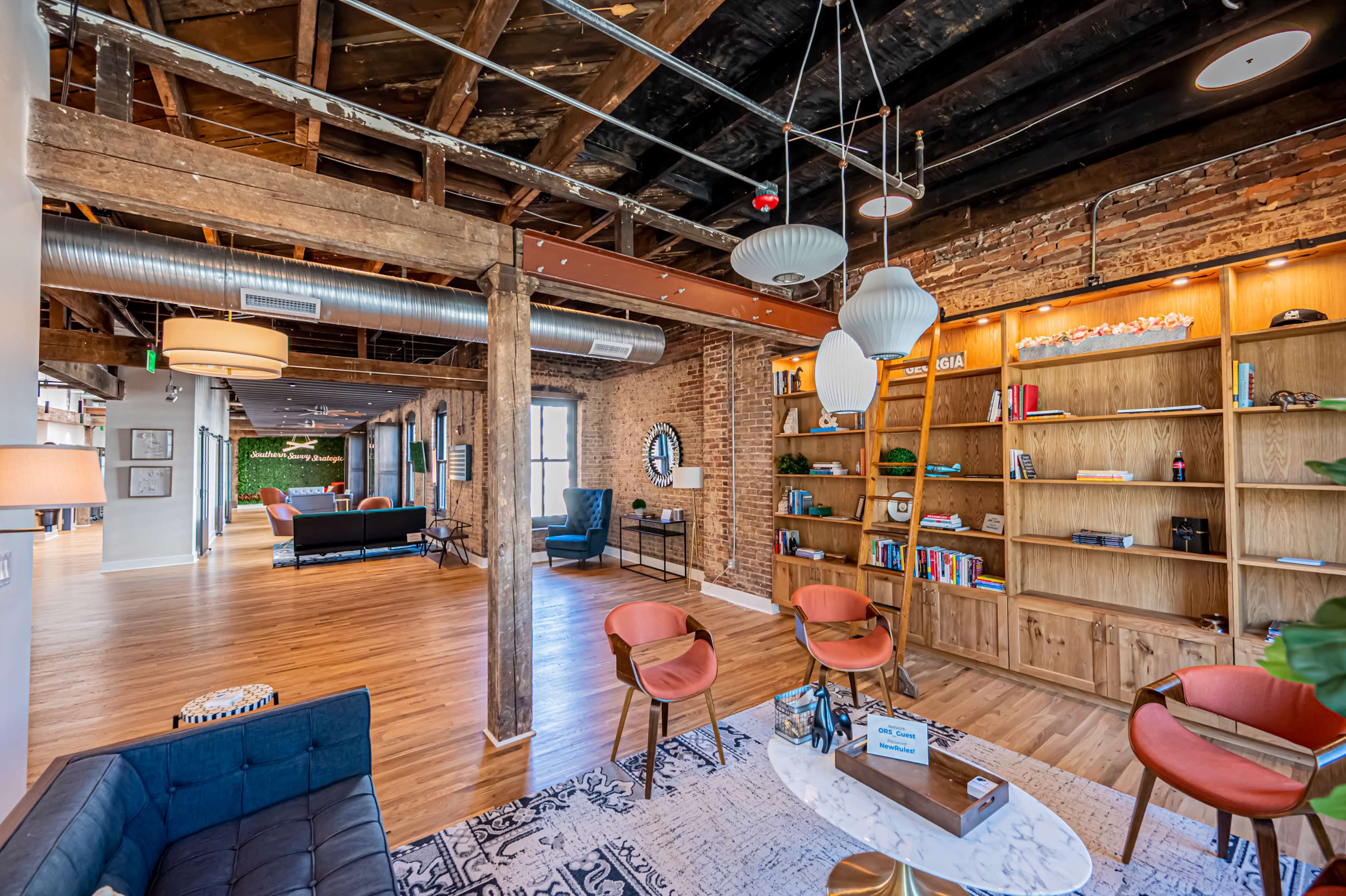 A modern office space with exposed wooden beams, a bookcase filled with books, and seating areas arranged for collaboration.