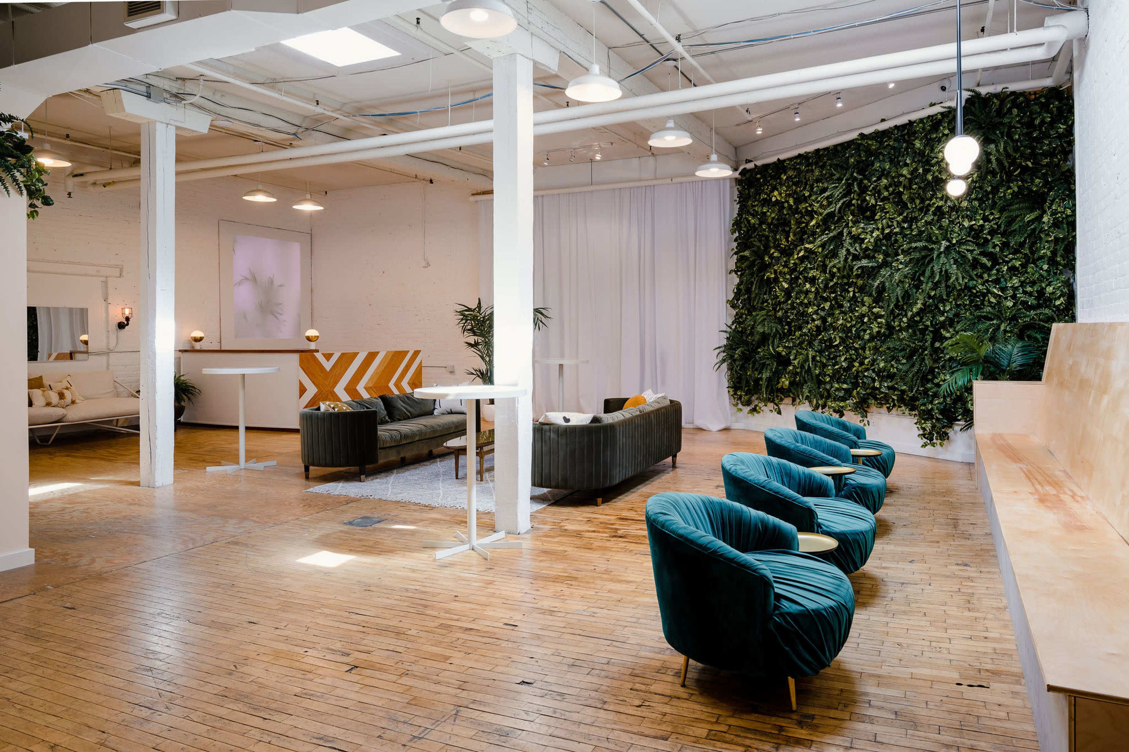 The image shows a spacious, modern lounge area with green seating, a vertical plant wall, and wooden floors.