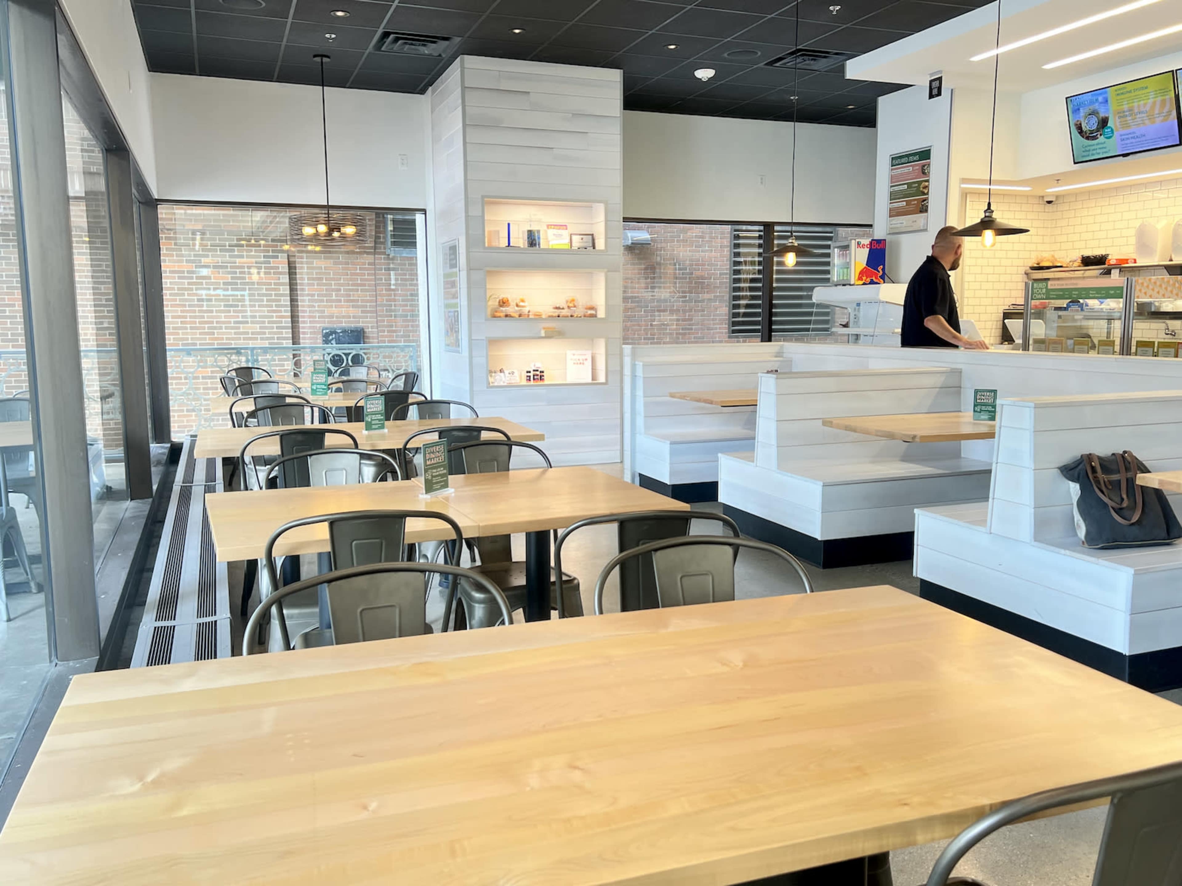 The image shows a modern café interior with wooden tables, metal chairs, and a service area in the background.