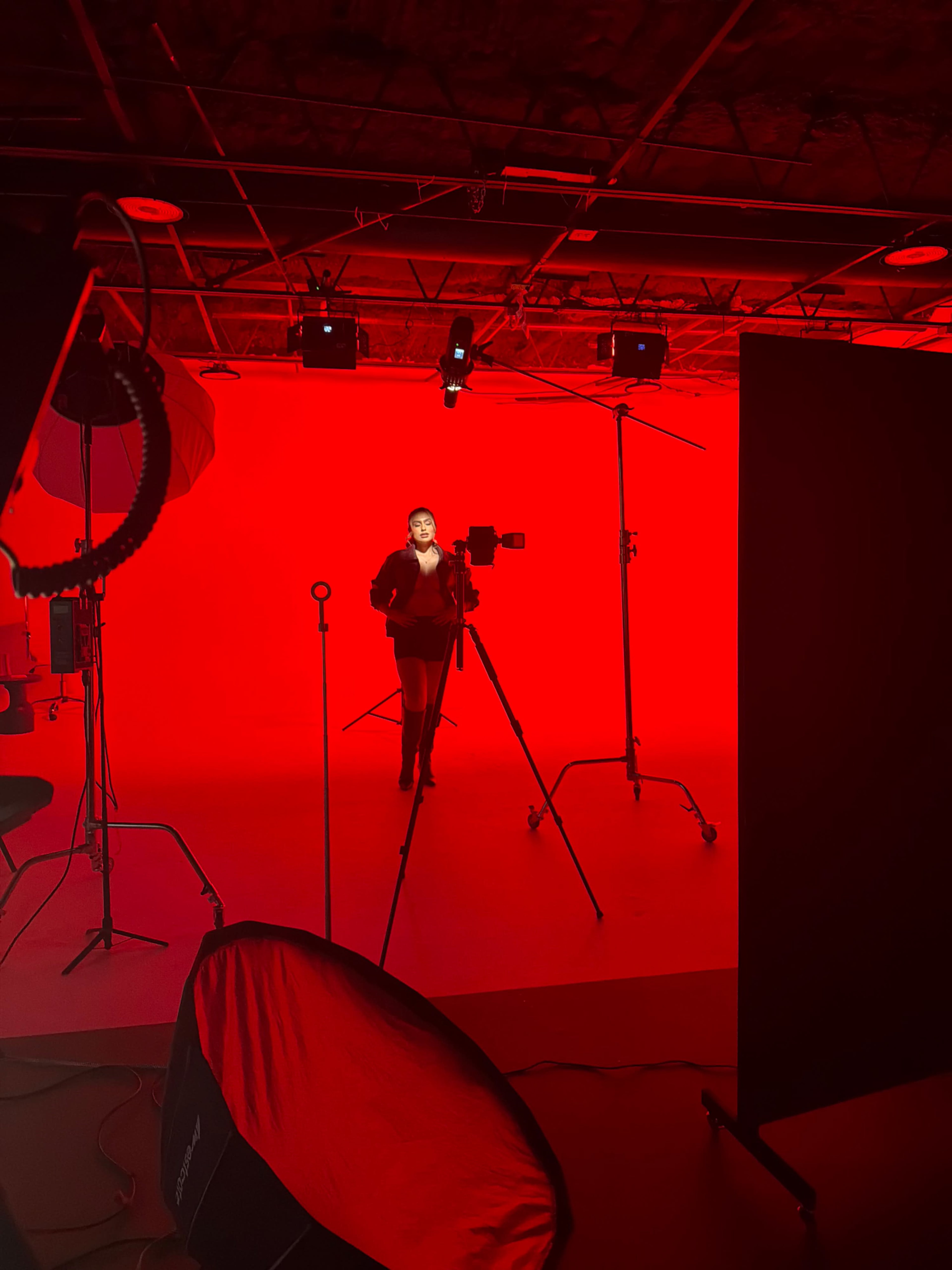 A person stands in a red-lit studio with a camera setup and various equipment visible in the foreground.