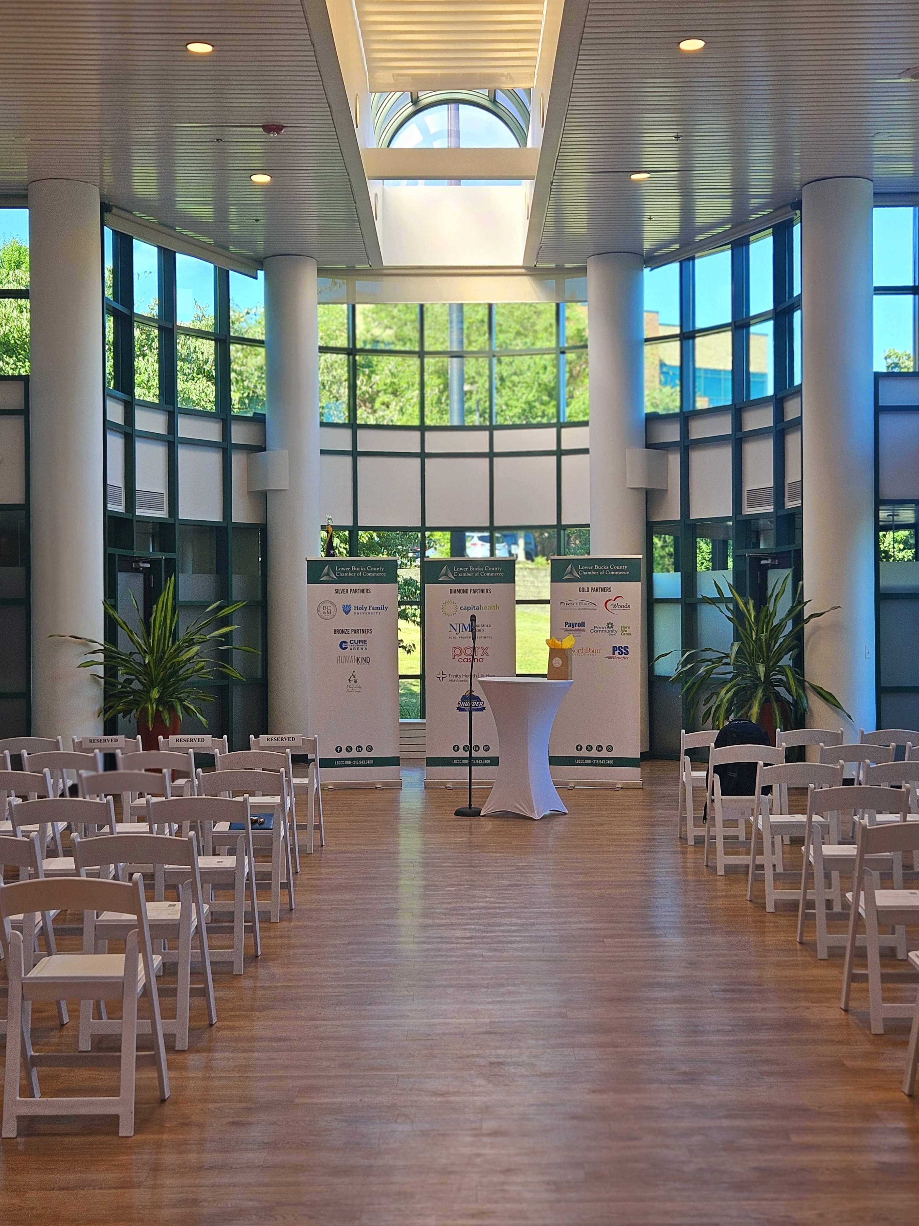A well-lit auditorium with rows of white chairs facing a small stage that has a podium and banners on either side.