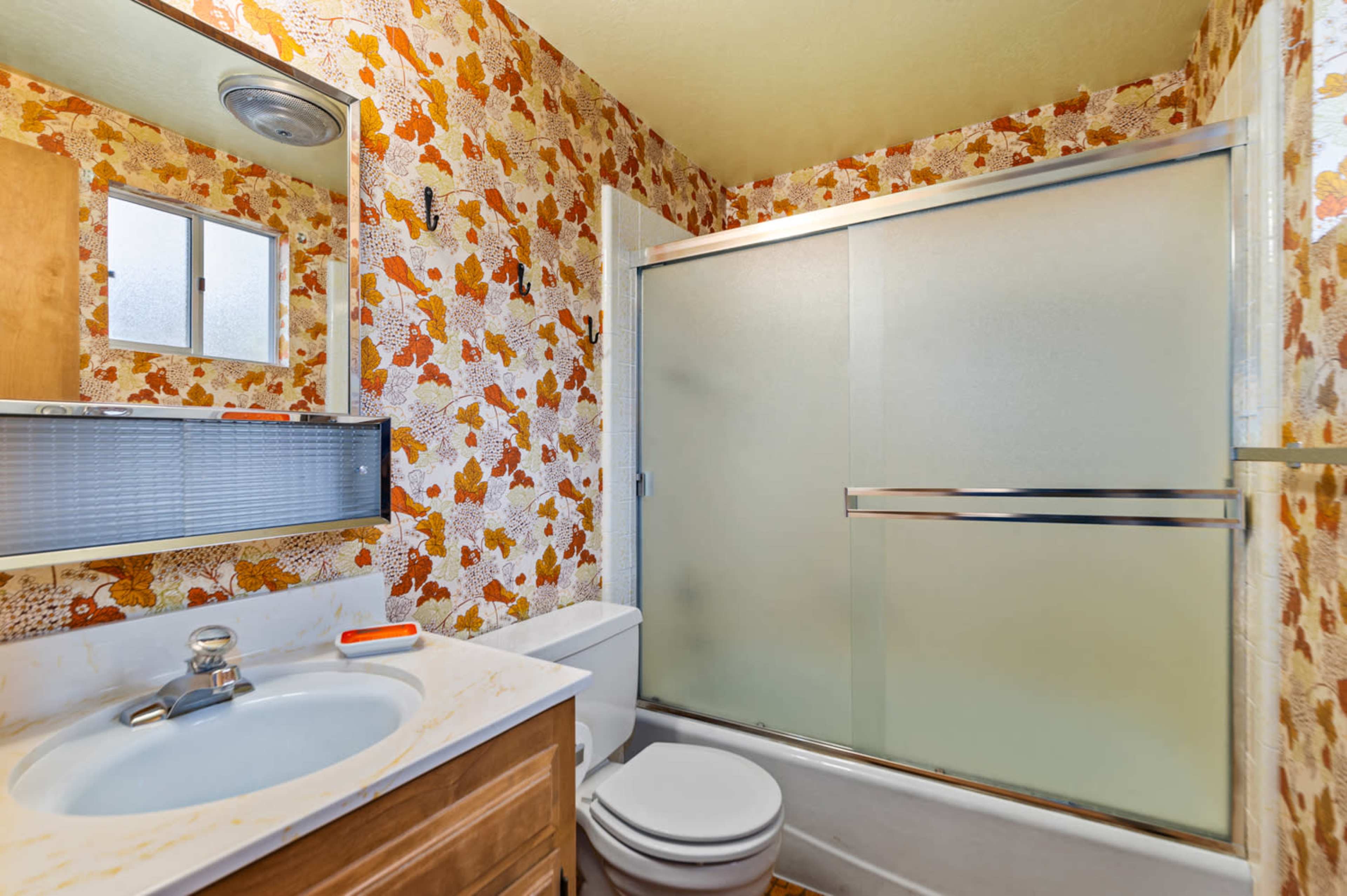 The bathroom features a shower enclosure with frosted glass, a toilet, and a sink with a marble countertop, all set against a backdrop of floral wallpaper.