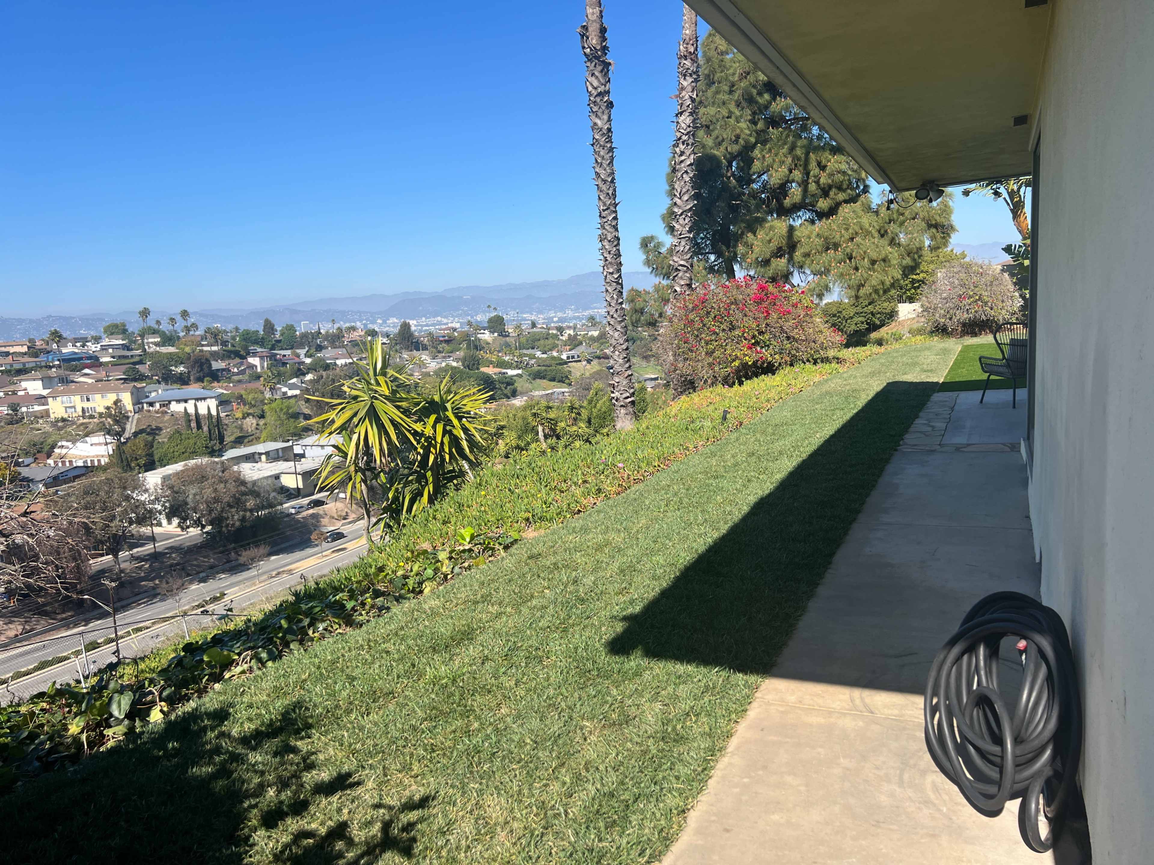 A view from a patio overlooking a landscaped yard and cityscape against a clear blue sky.