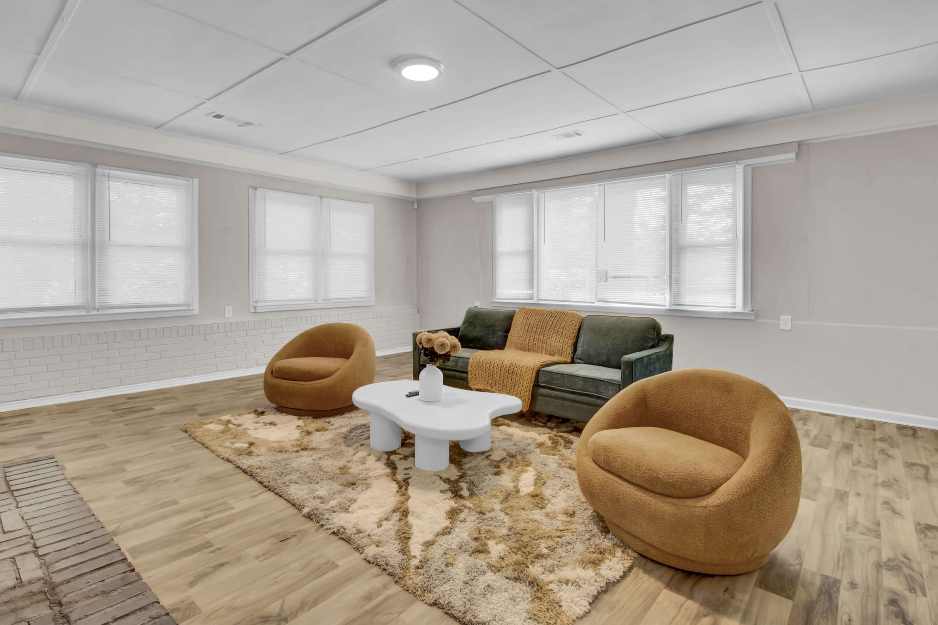 The image shows a living room with a green sofa, two orange armchairs, a white coffee table, and large windows allowing natural light.
