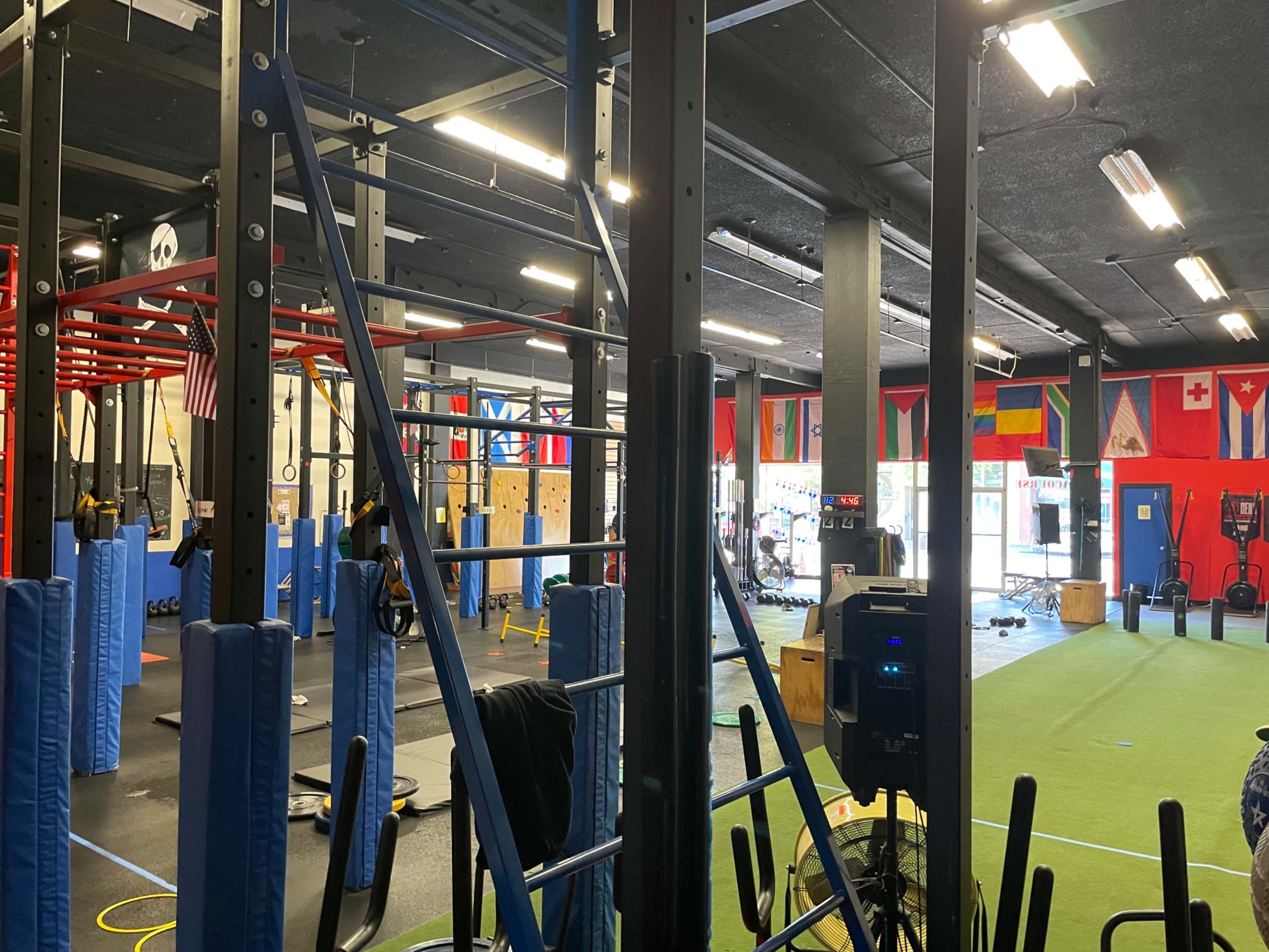 The image shows a gym interior featuring various fitness equipment, exercise mats, and wall-mounted flags from different countries.
