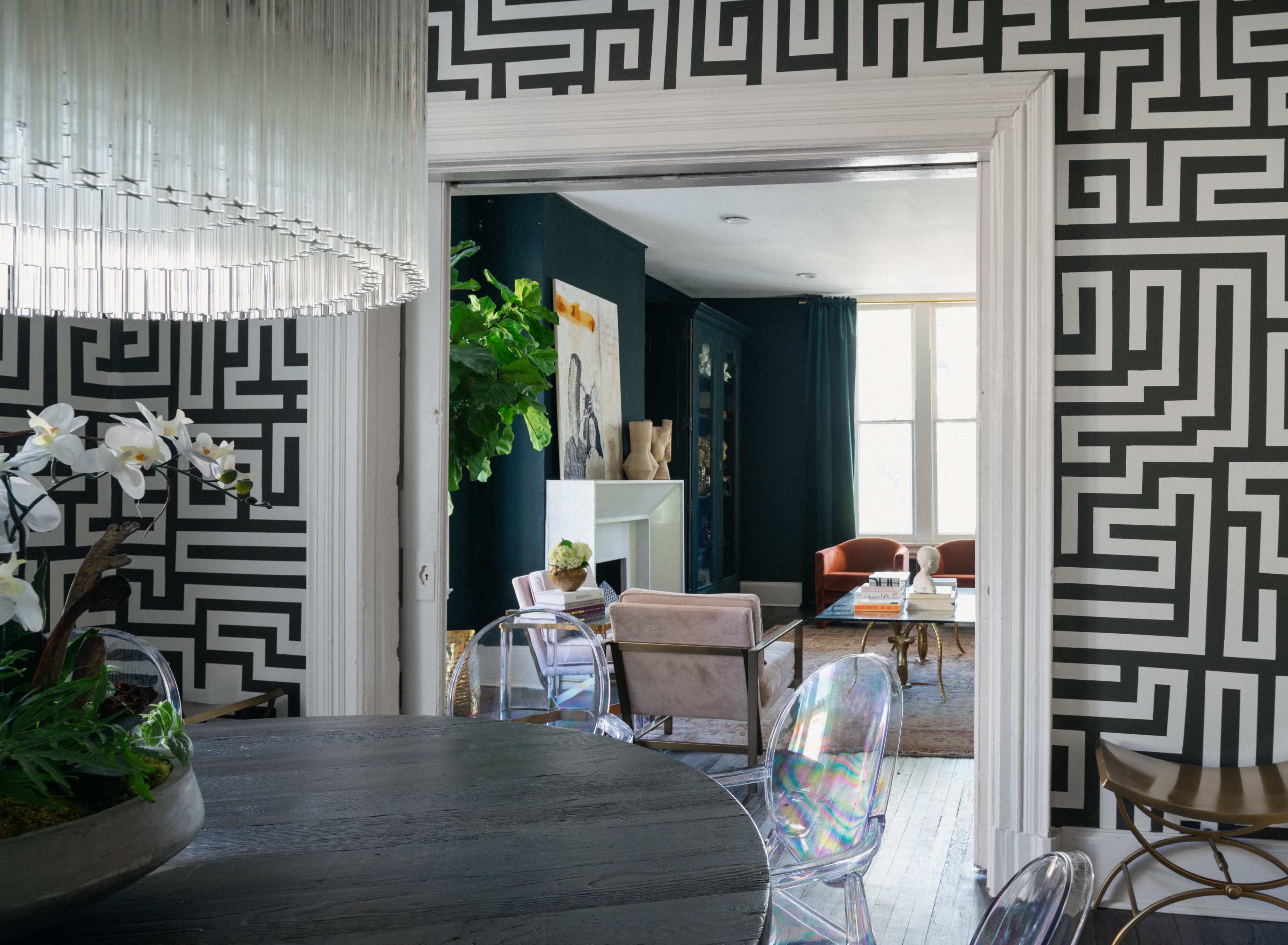 A dining area with a black and white geometric patterned wall opens into a living space featuring a mix of modern furniture and decor.