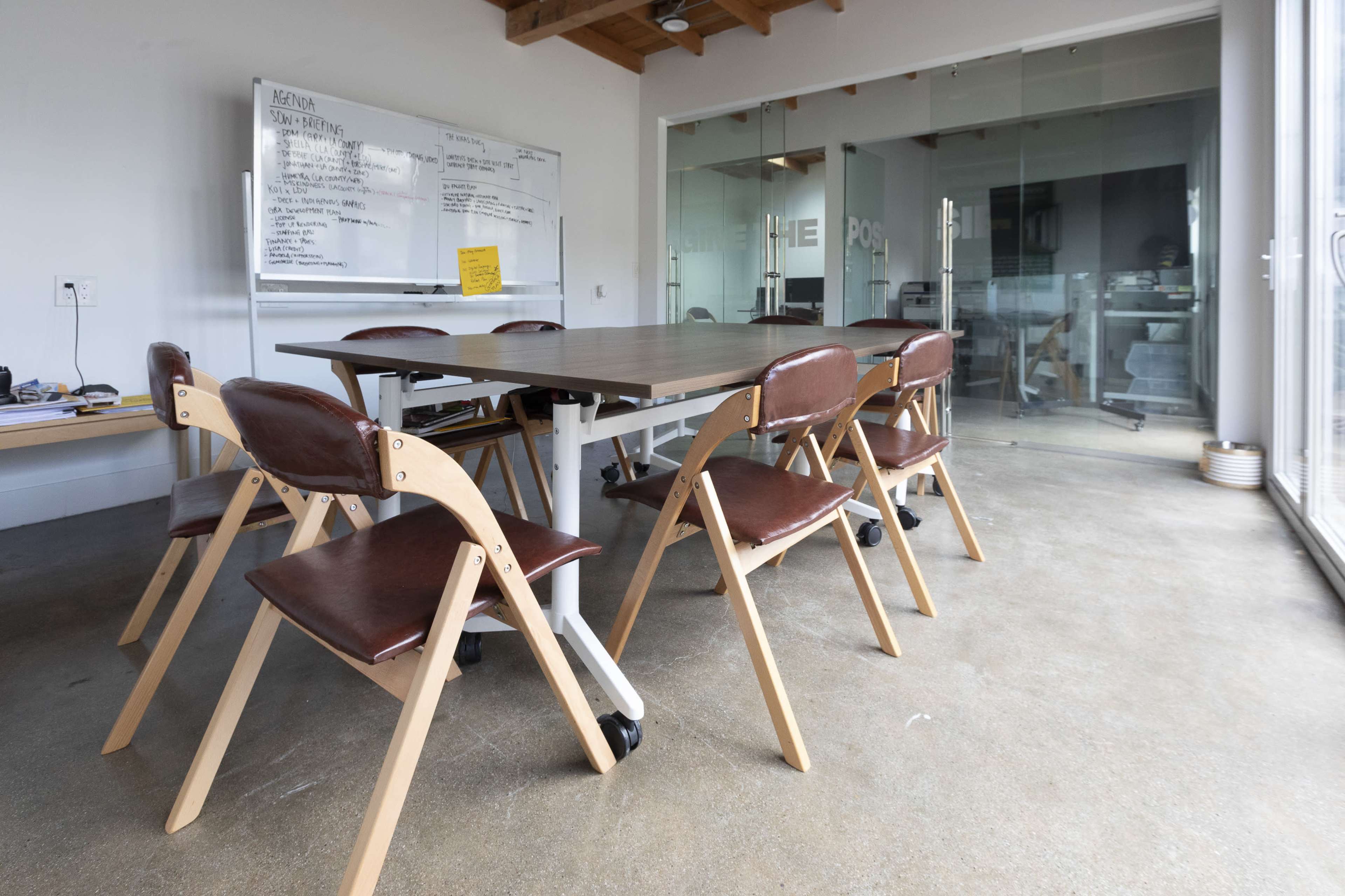 A conference room with a large table surrounded by wooden folding chairs, and glass walls showcasing a collaborative workspace.