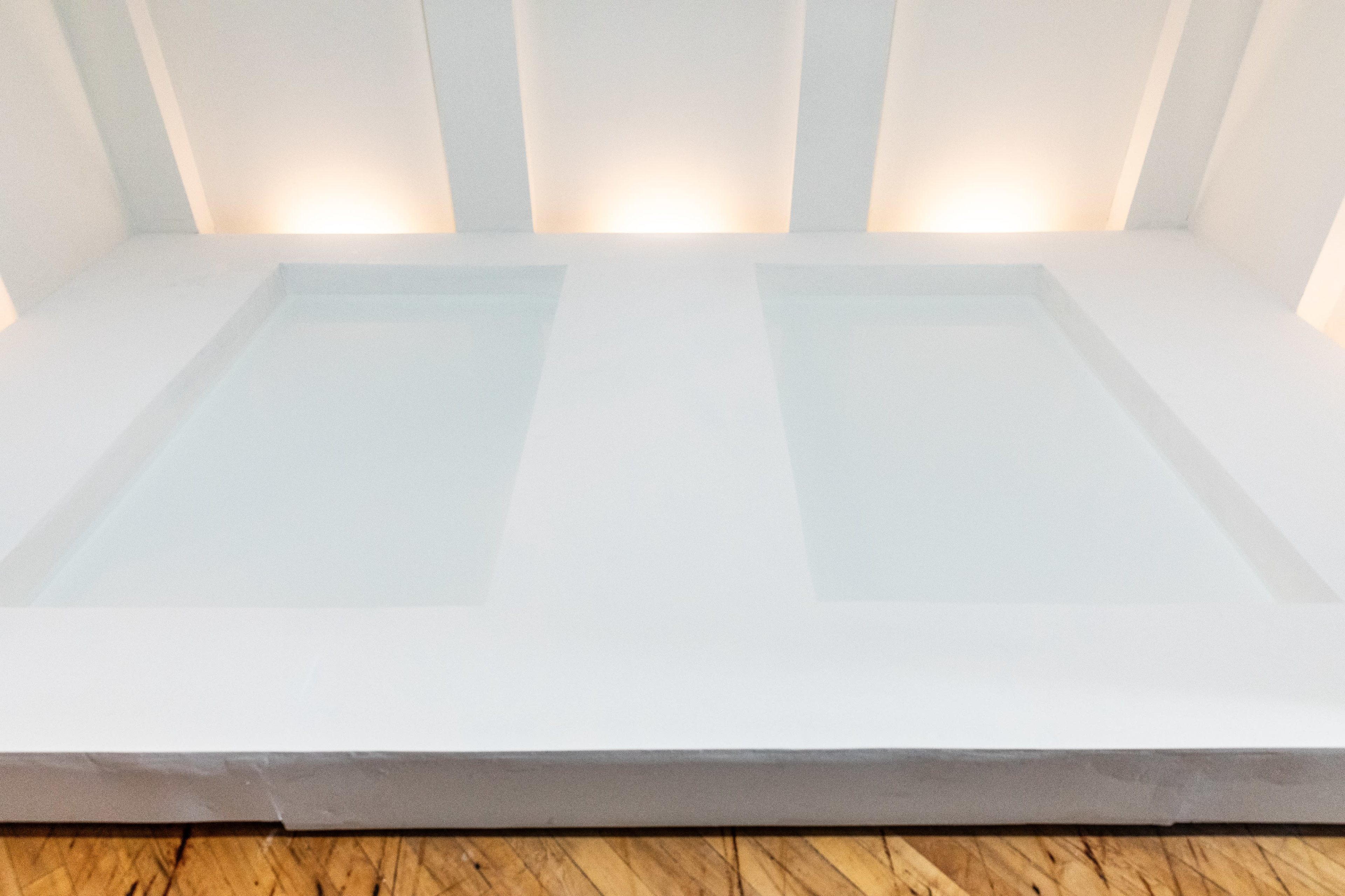 The image shows a minimalist, white room featuring two shallow, rectangular pools of clear water.