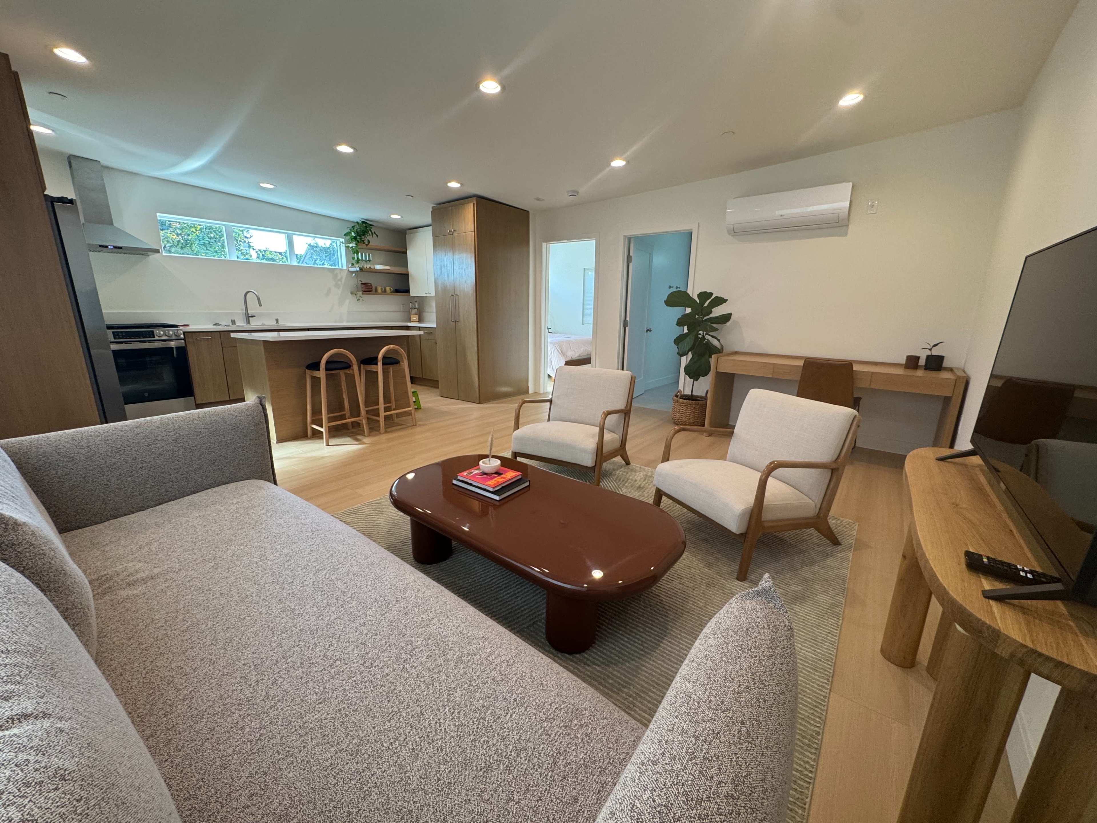 The image shows a modern living area with a sofa, two chairs, a coffee table, and a kitchenette in an open-concept layout.