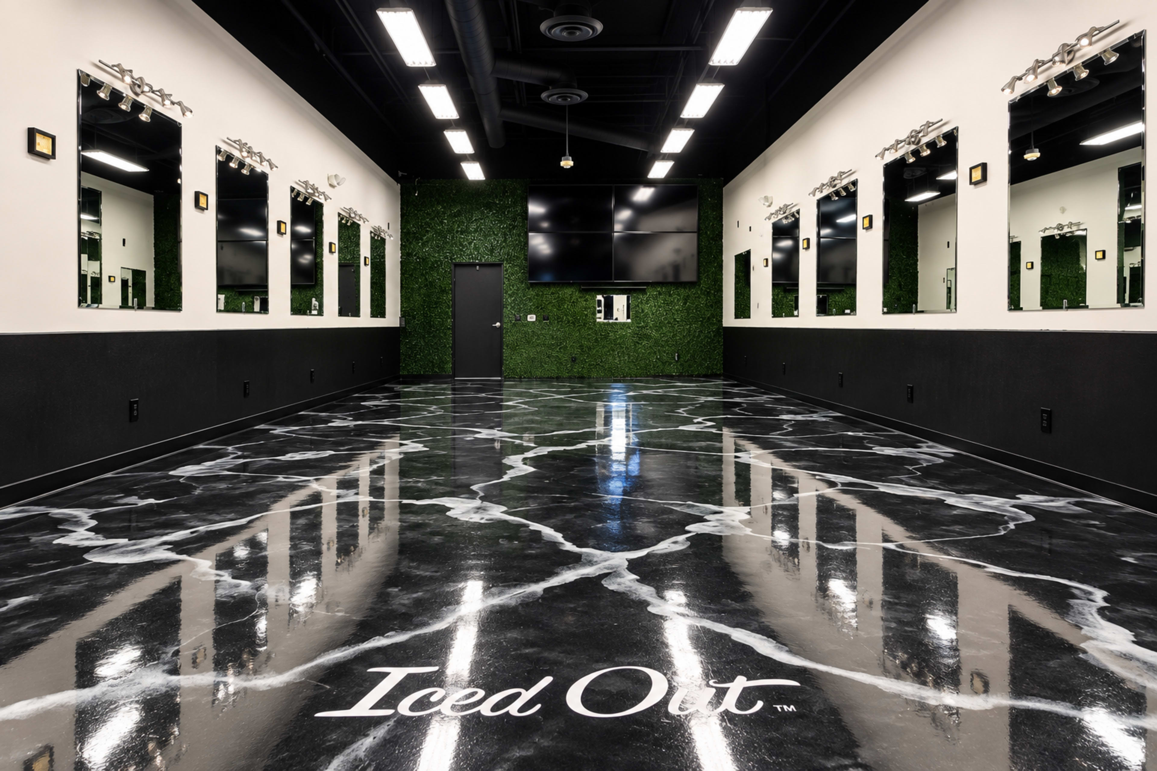 The interior of a modern grooming or beauty salon features black marble-patterned flooring, a green wall, multiple mirrors, and a large screen on the wall.