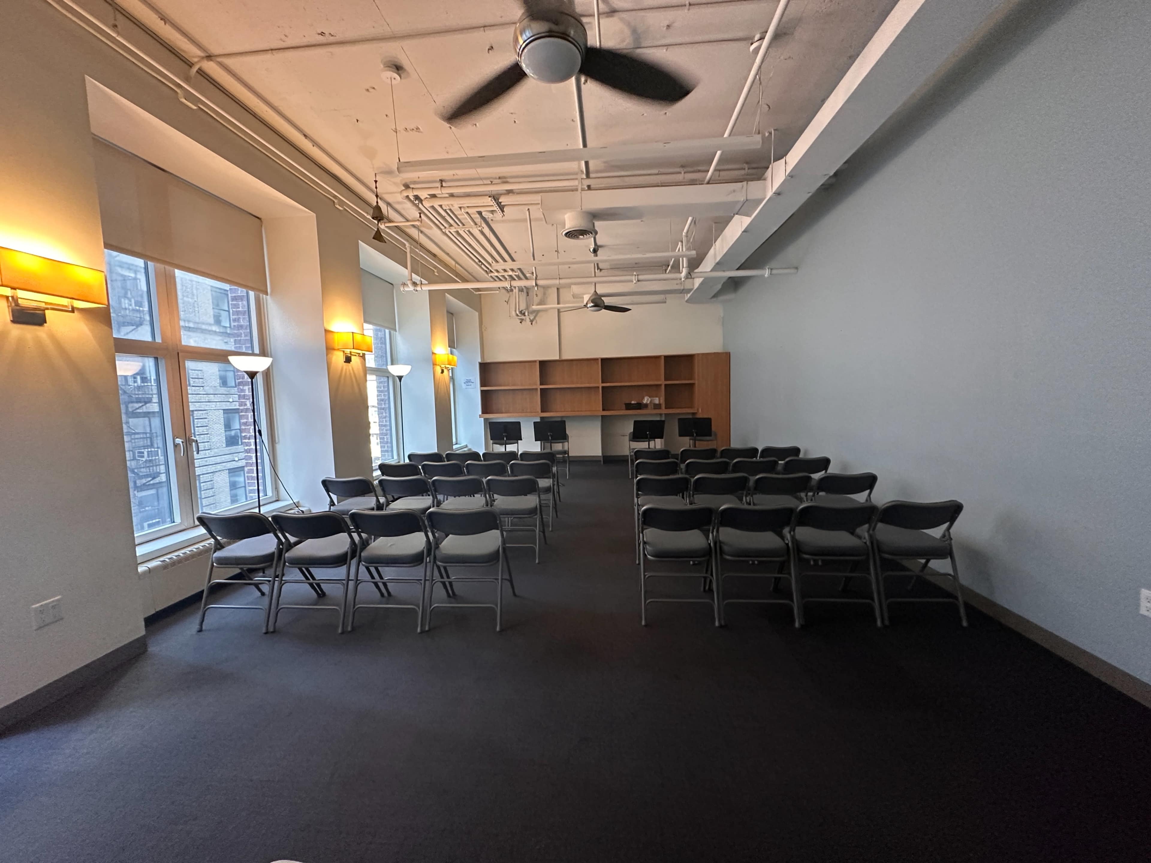 A meeting room features rows of chairs facing a counter area, illuminated by natural light from large windows.