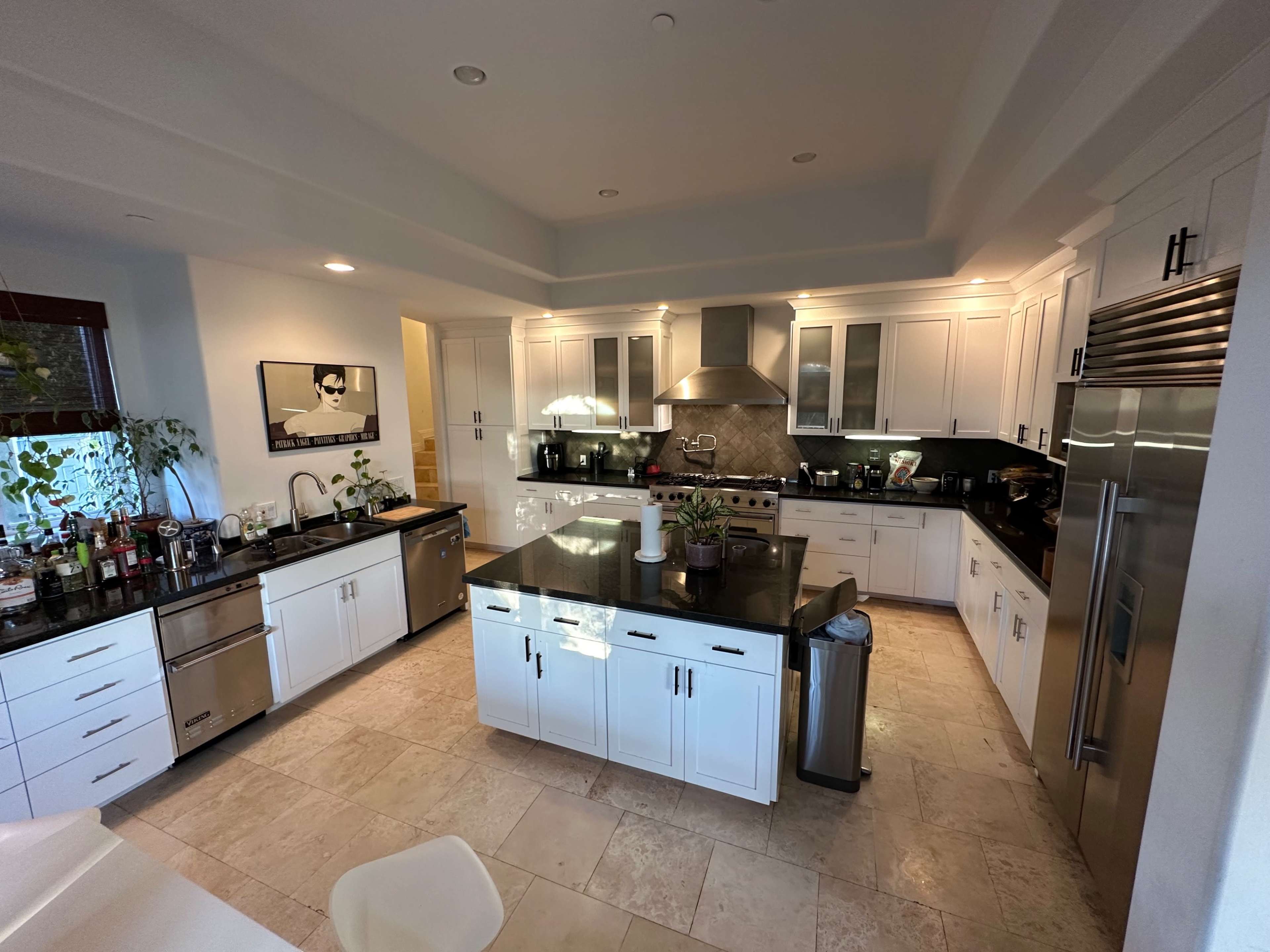 A modern kitchen features white cabinetry, a central island, stainless steel appliances, and dark countertops.