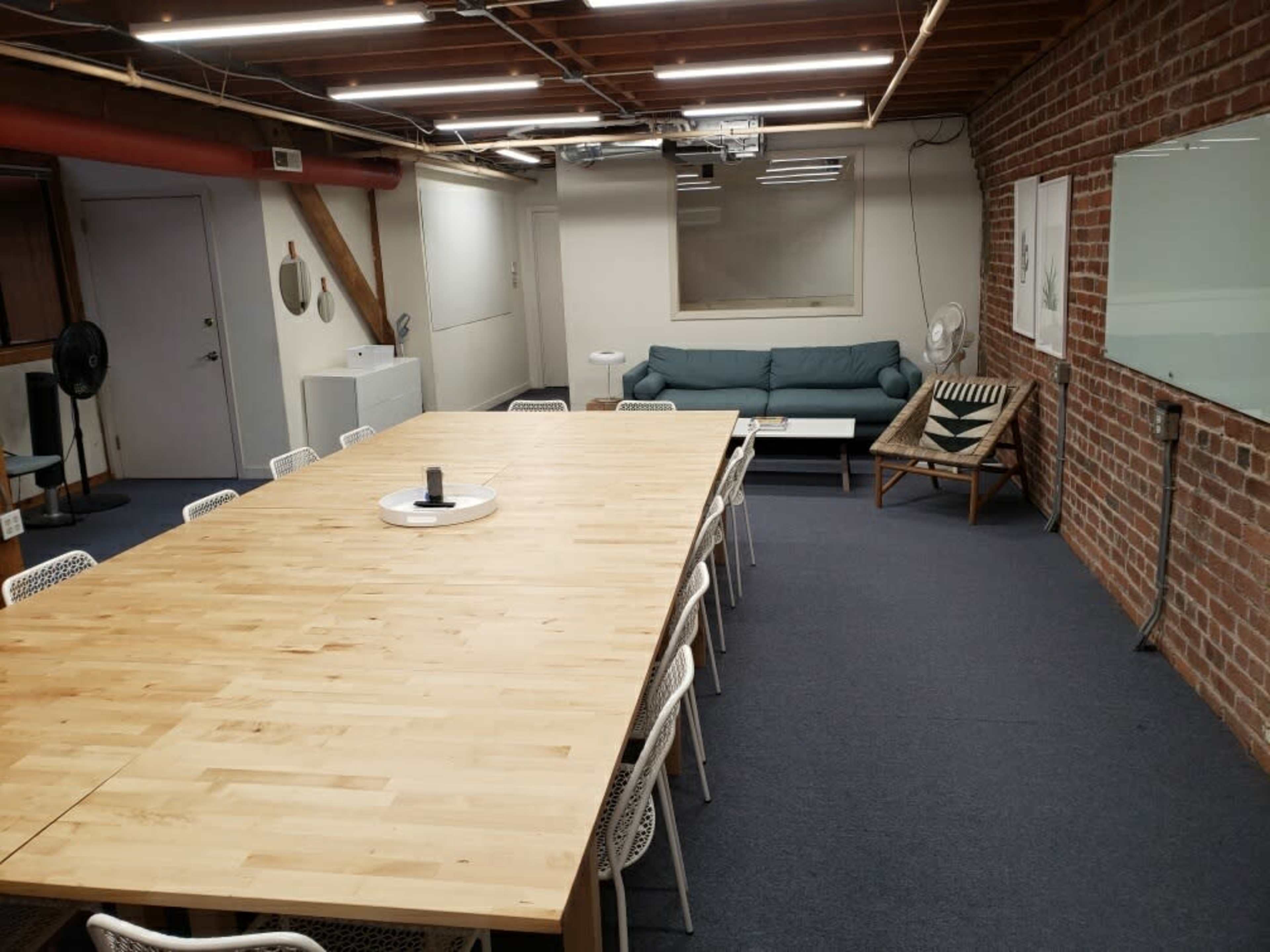 A large, wooden conference table is surrounded by white chairs in a spacious room with brick walls and a green couch in the corner.
