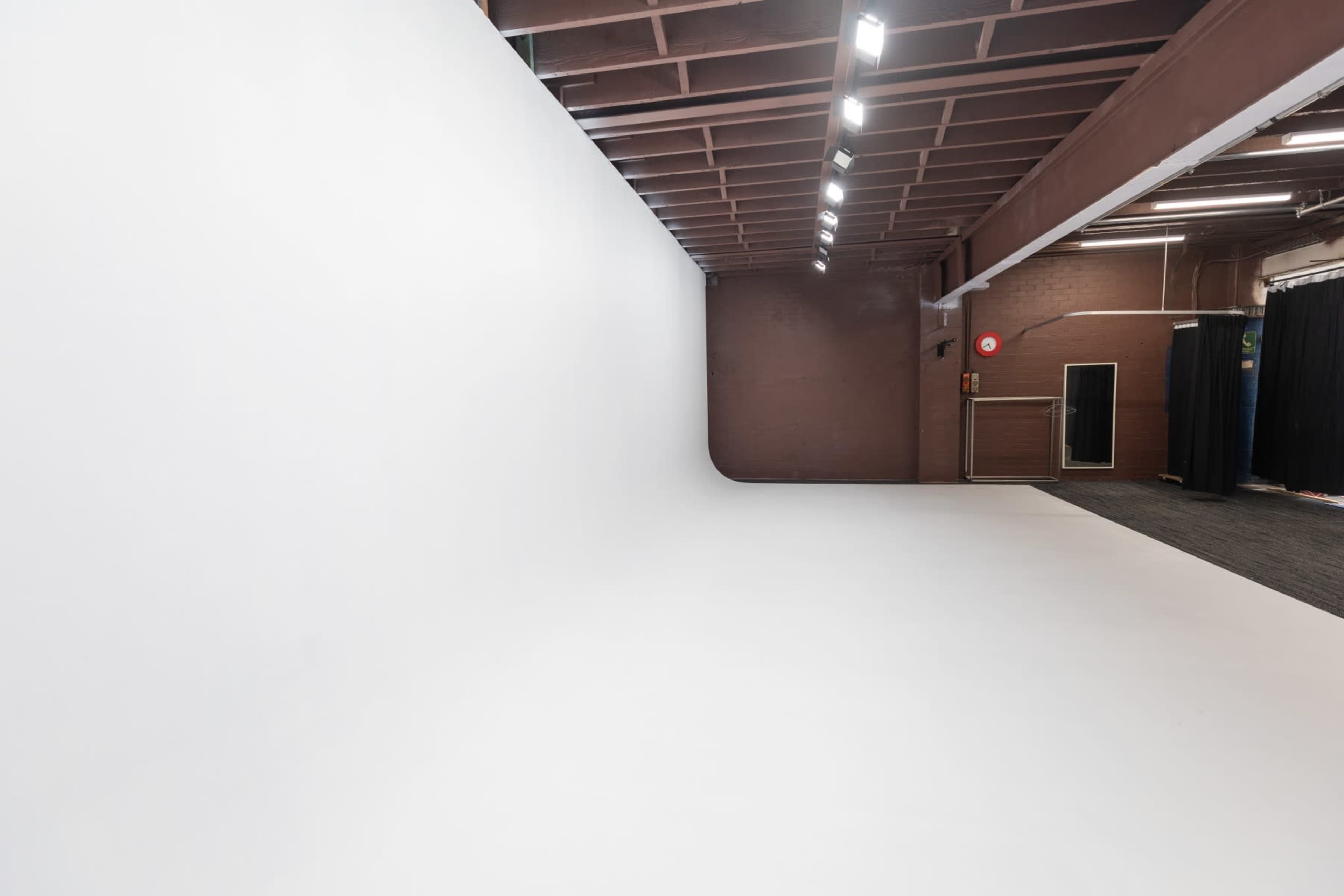 The image shows a spacious, empty studio with a seamless white backdrop and overhead lighting.