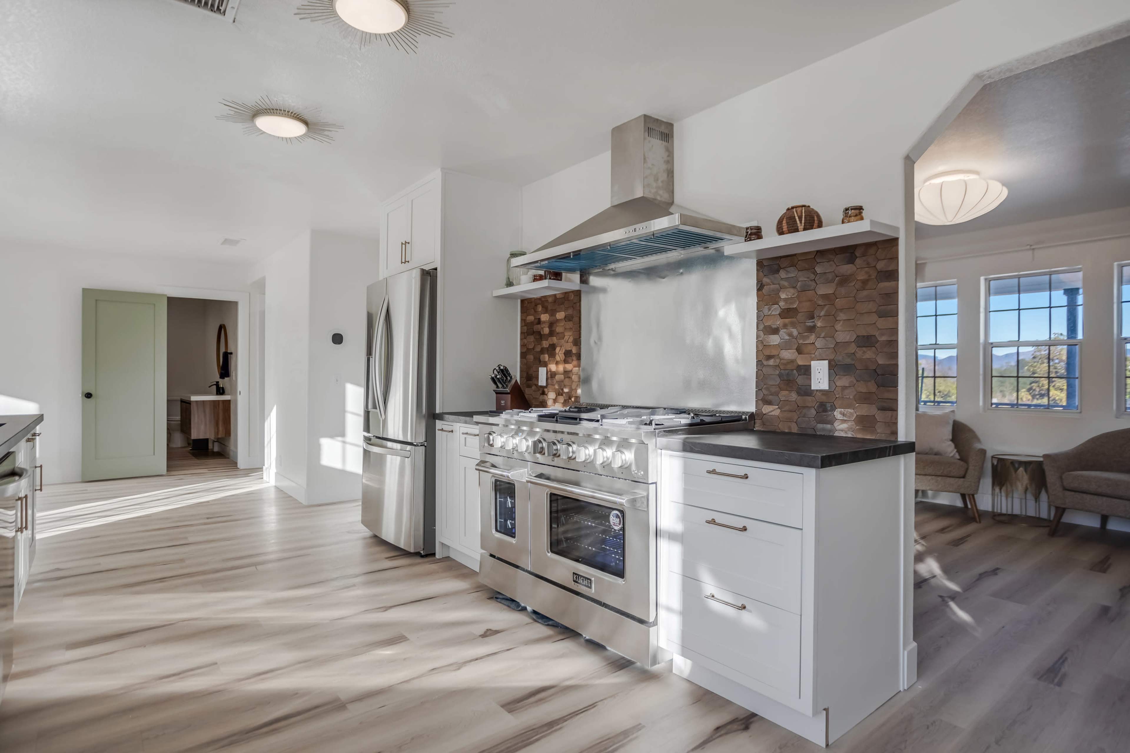 A modern kitchen features stainless steel appliances, a stone backsplash, and light wood flooring.