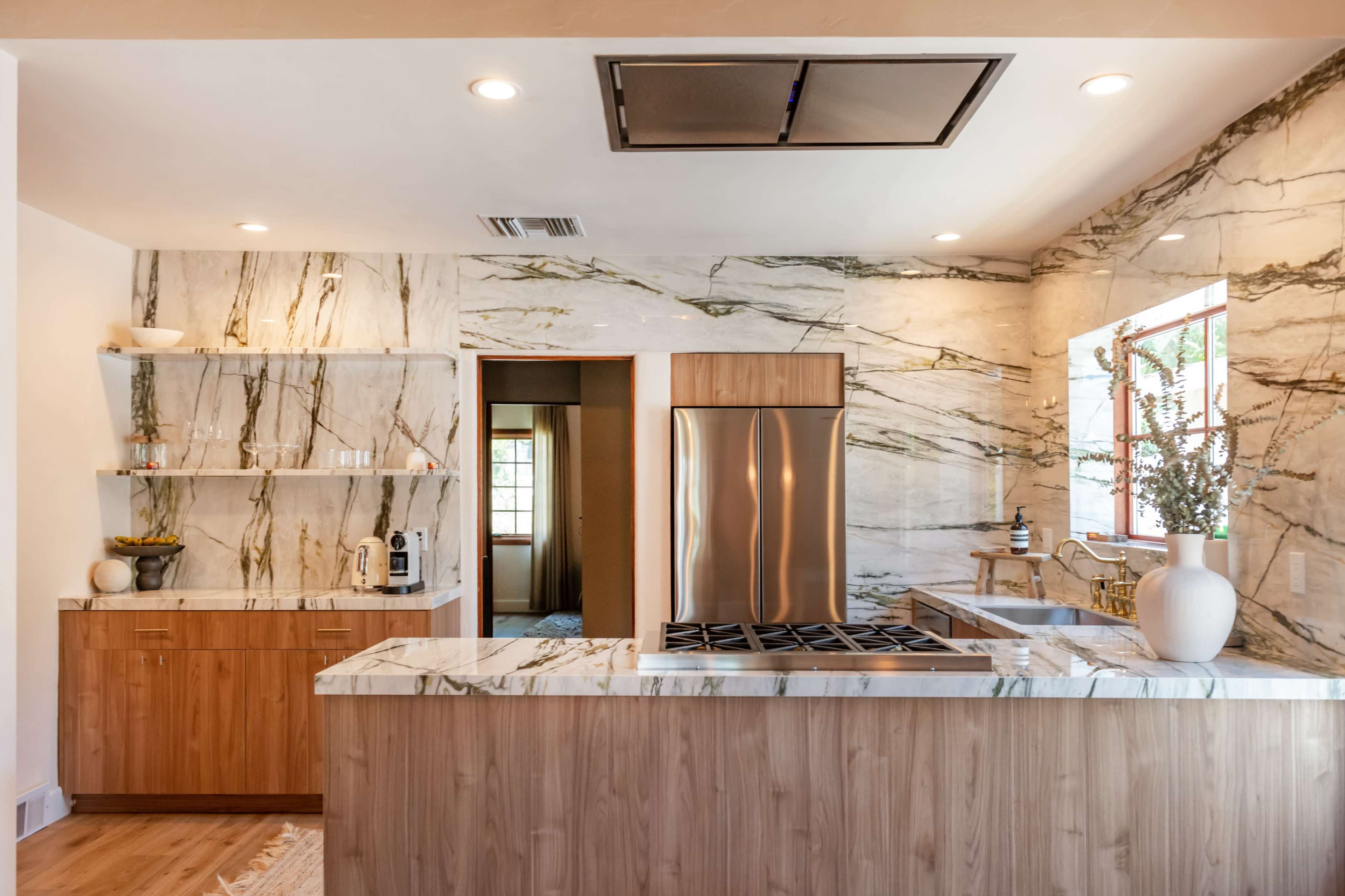 A modern kitchen features marble walls, a stainless steel refrigerator, and a kitchen island with a gas stove.