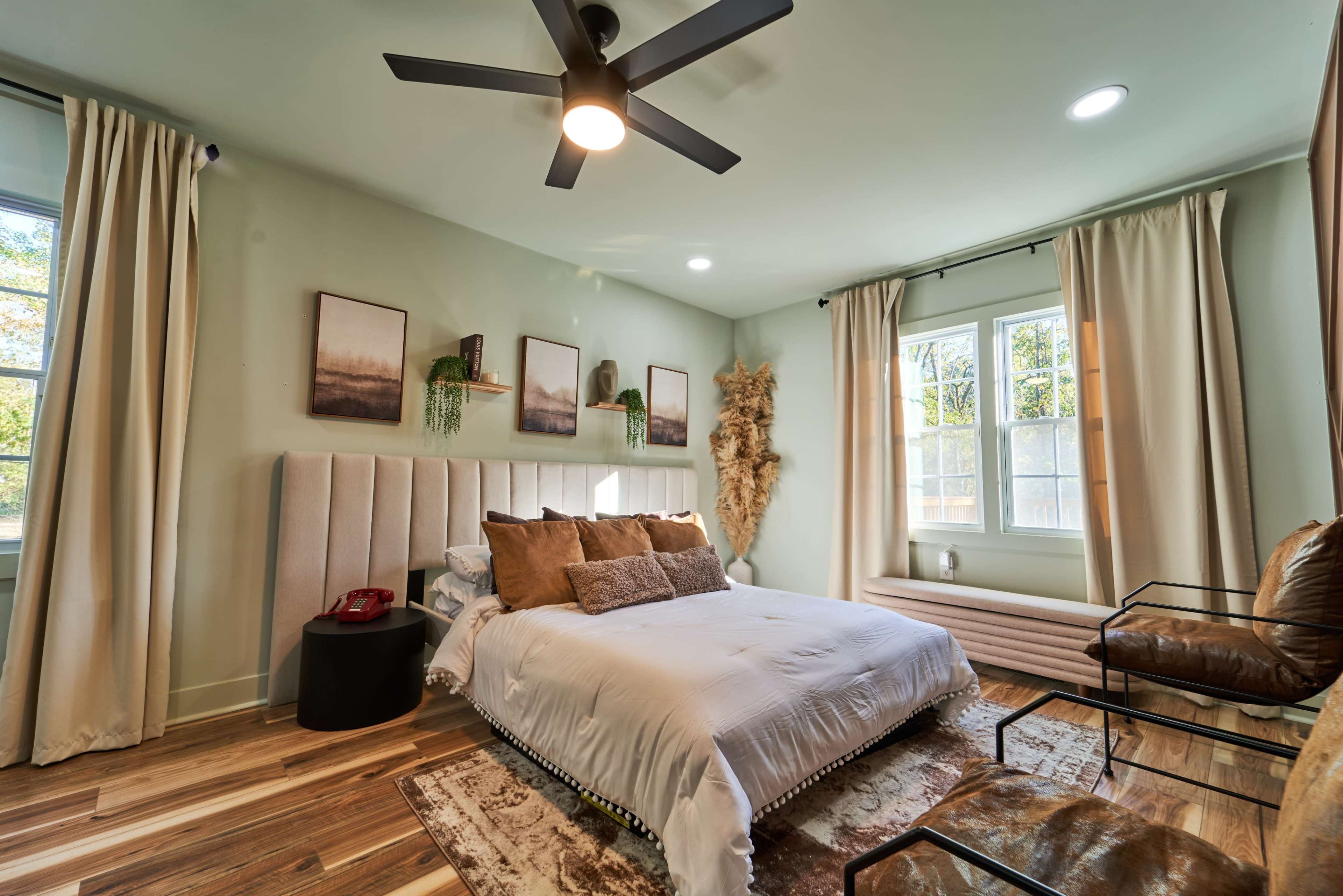 The bedroom features a light green color scheme with a bed, a nightstand, two windows, and decorative wall art.