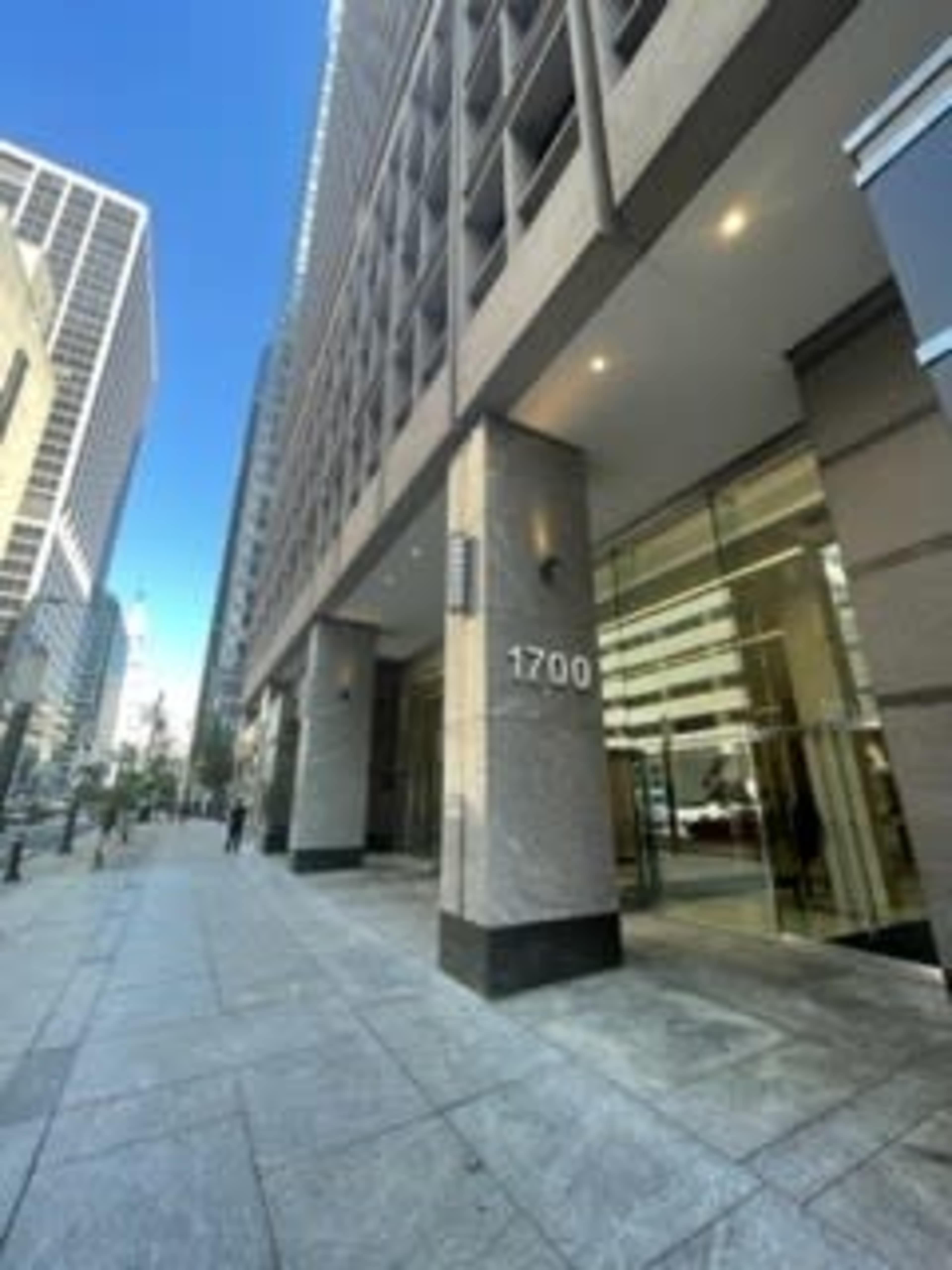 The image shows the entrance of a commercial building located at 1700, with a wide sidewalk and a clear blue sky.