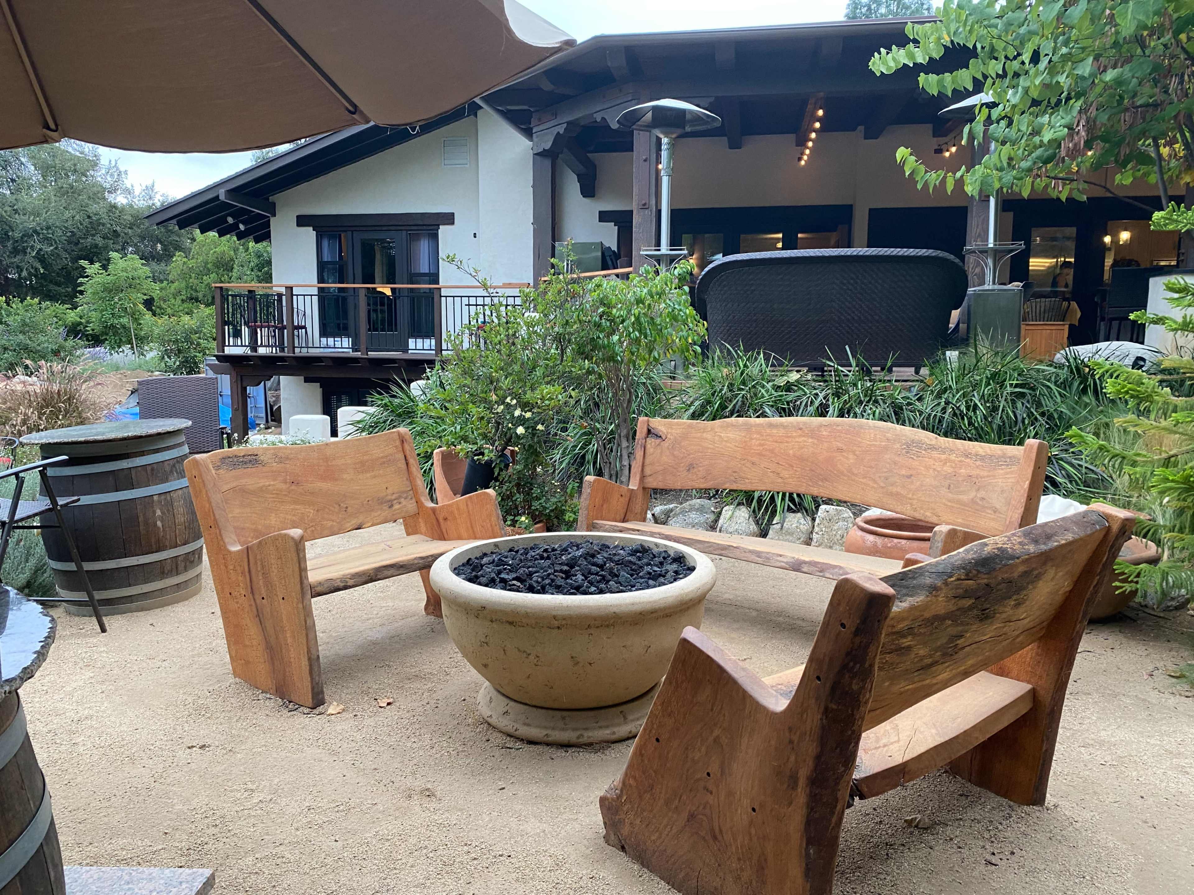 A circular seating arrangement made of wooden benches around a stone fire pit in a garden setting.