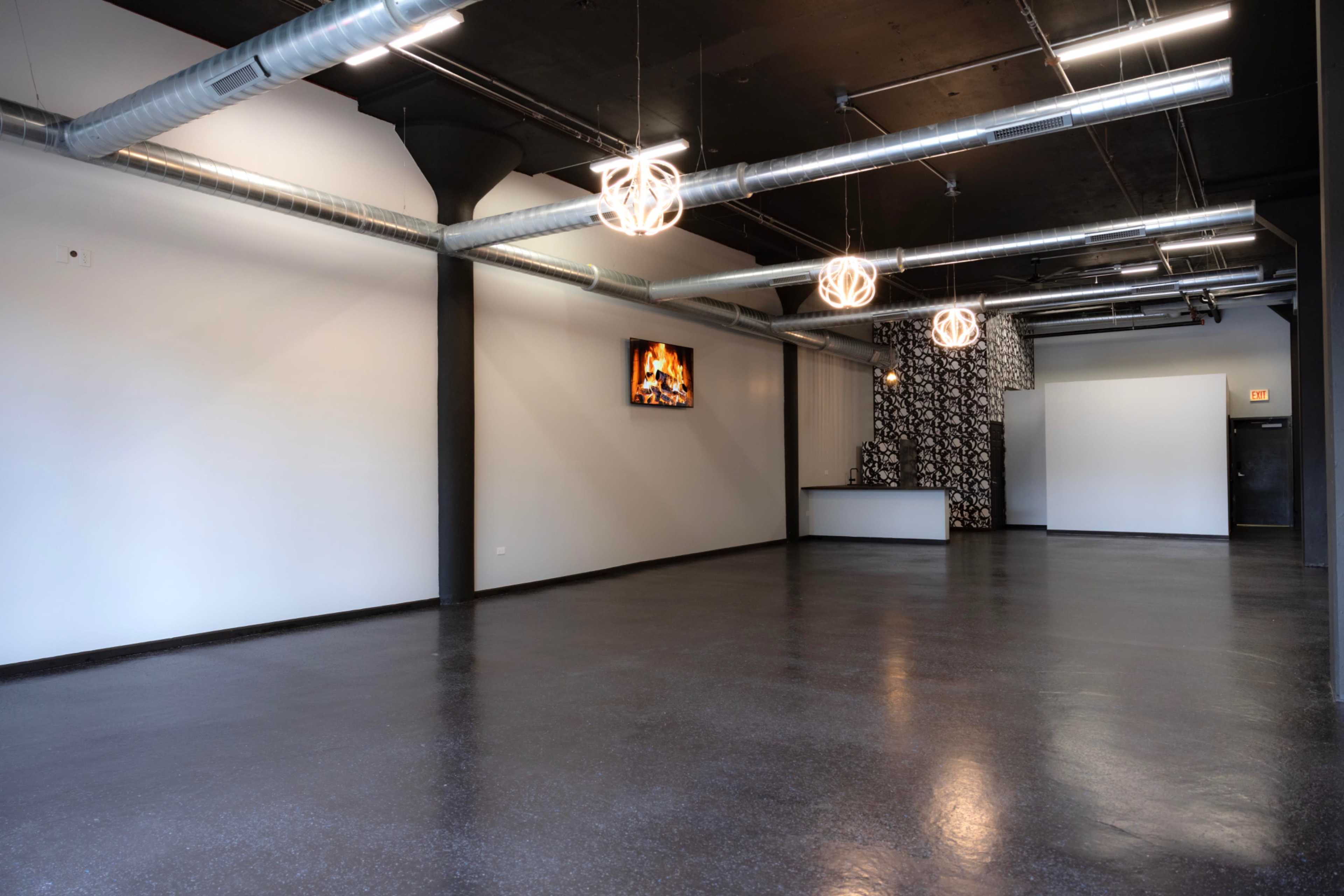 The image shows an empty room with polished dark flooring, exposed ductwork, and decorative lighting fixtures.