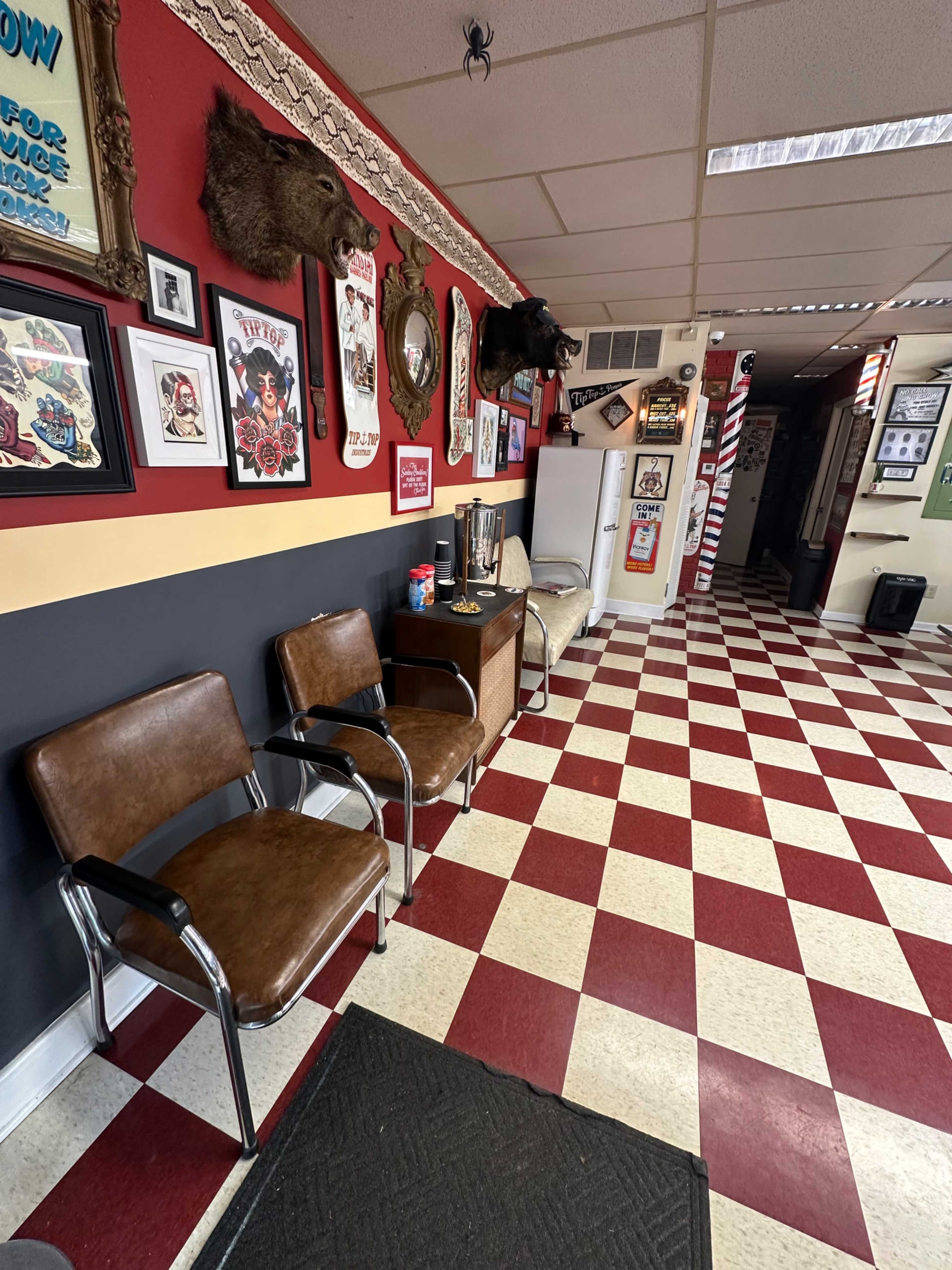 The image shows a barbershop interior with red and black walls, checkerboard flooring, and various framed artworks, including taxidermy decorations.