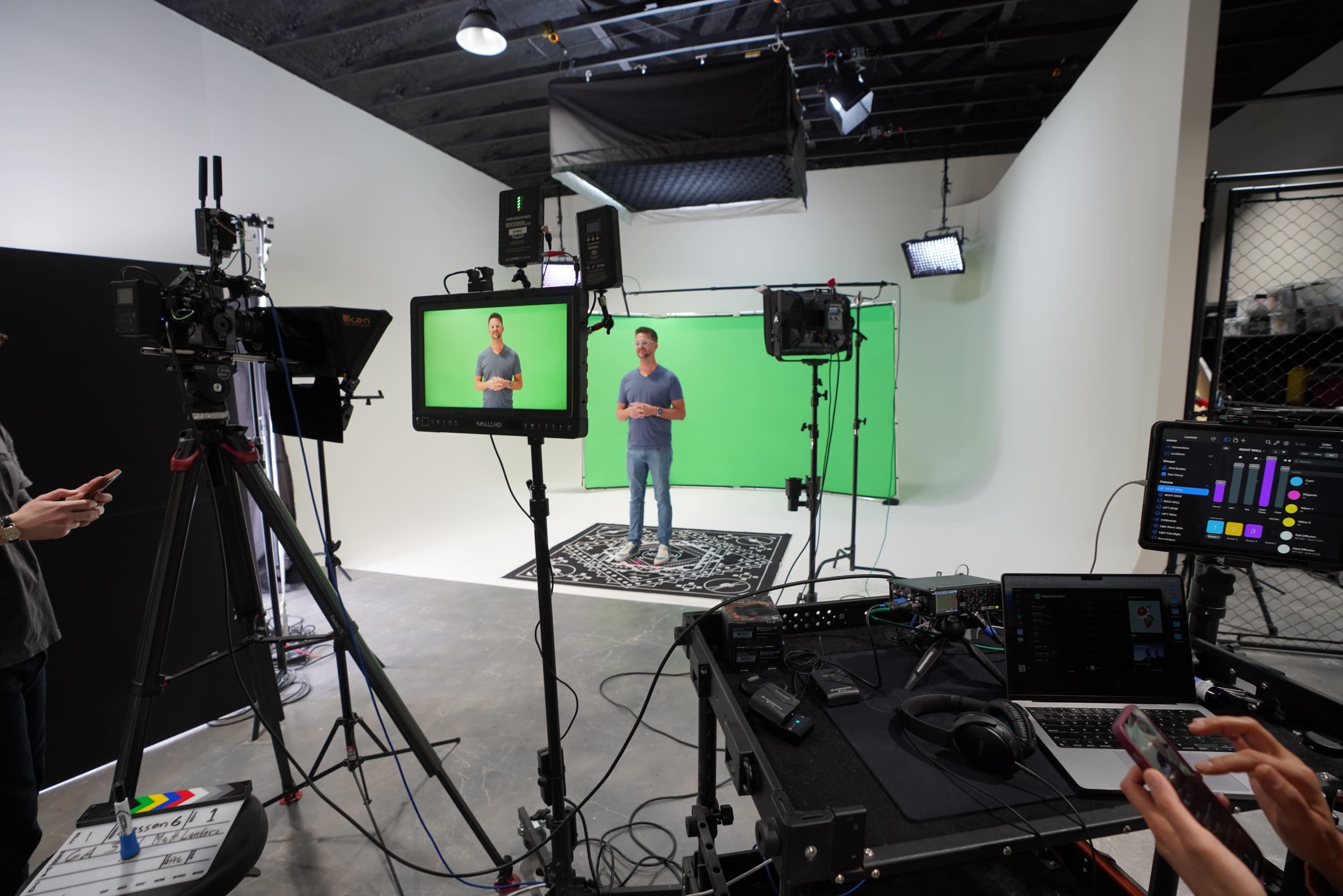 A person stands in front of a green screen, surrounded by video equipment and lighting in a studio setting.
