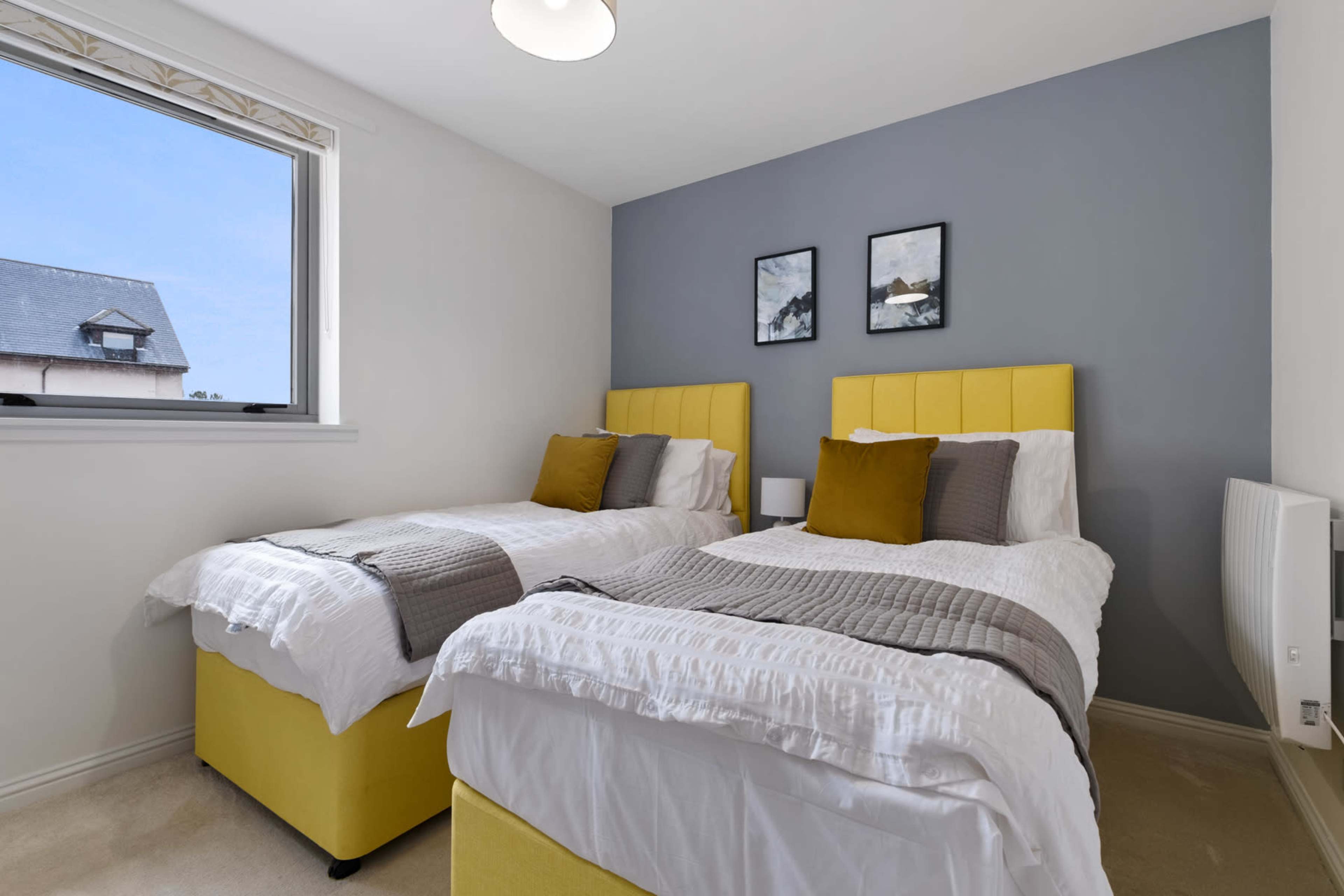 A bedroom with two yellow upholstered twin beds, each topped with white bedding and a gray throw, and framed artwork on the wall above.