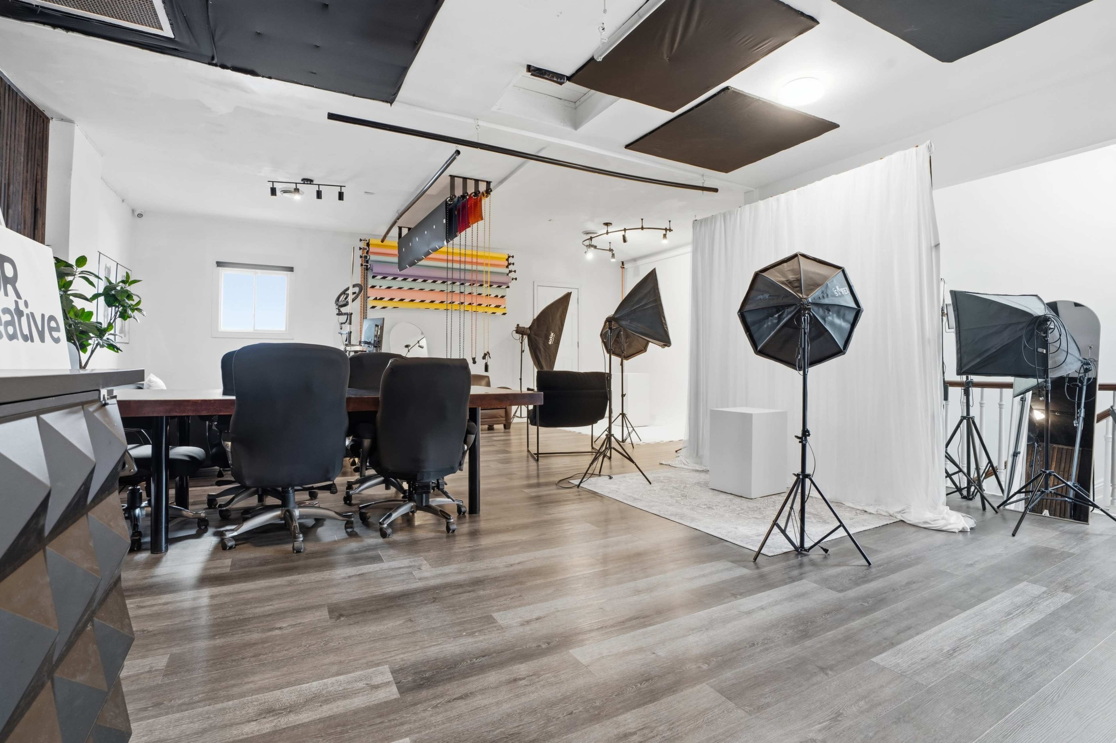 The image shows a modern studio space with several black office chairs, a long table, and multiple photography lights set up in a well-lit environment.