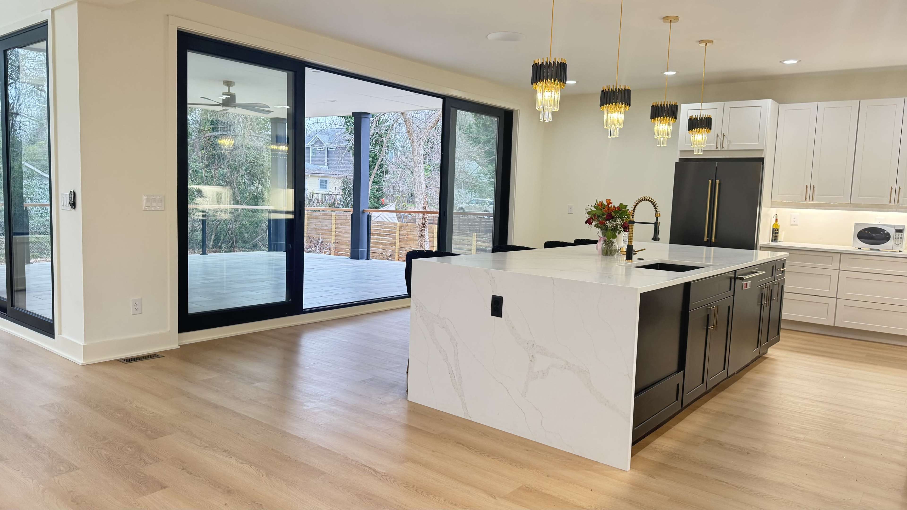 The image shows a modern kitchen featuring a large island with a marble countertop, dark cabinetry, and ample natural light spilling in from adjacent sliding glass doors leading to a patio.