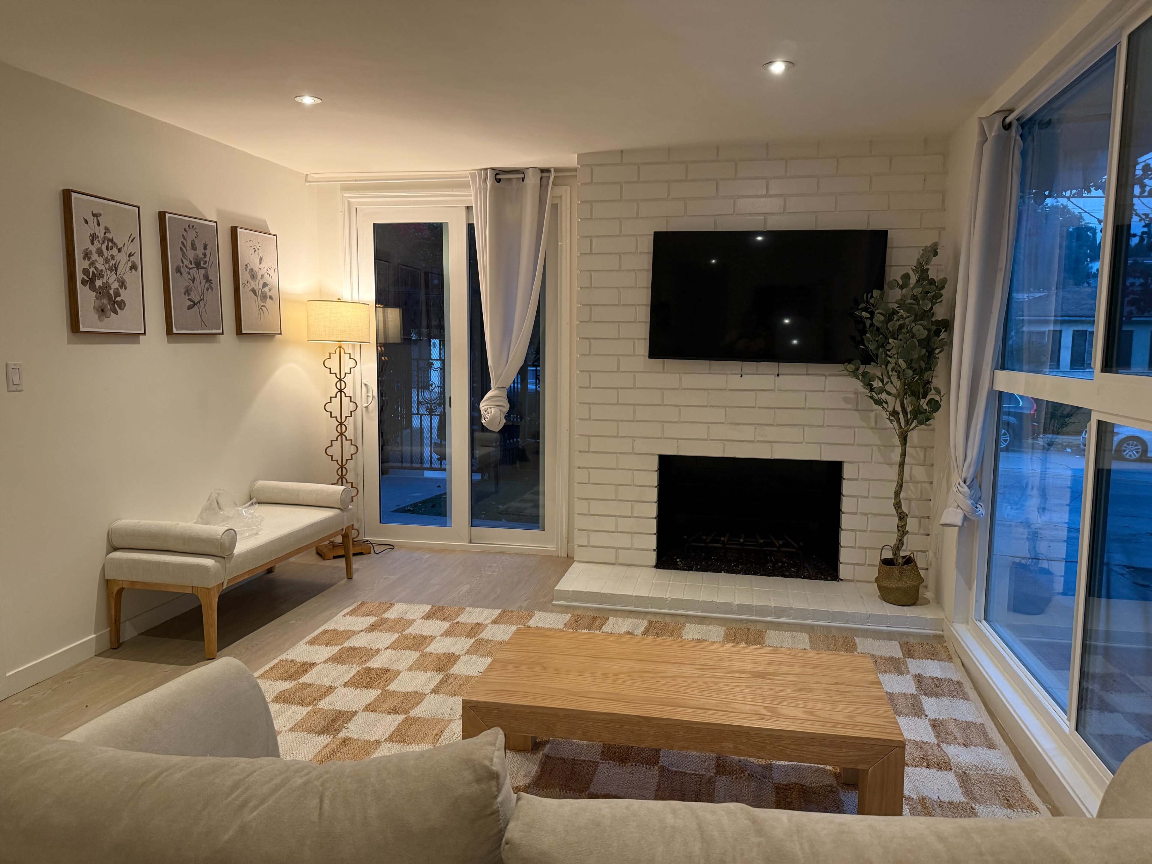 The living room features a light-colored sofa, a wooden coffee table, a brick fireplace, and a wall-mounted television.