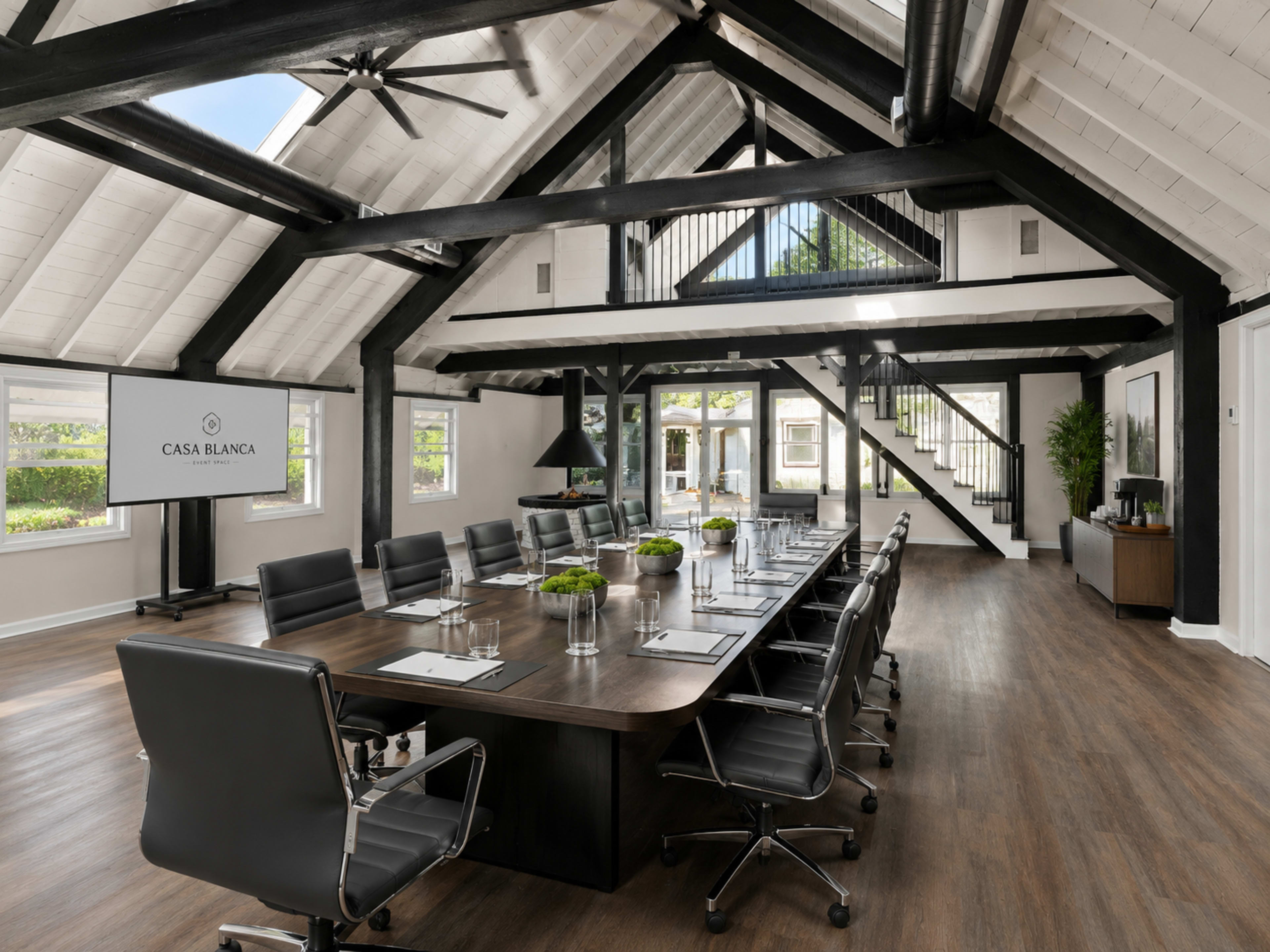 A spacious conference room features a long wooden table surrounded by black chairs, with large windows and modern design elements.