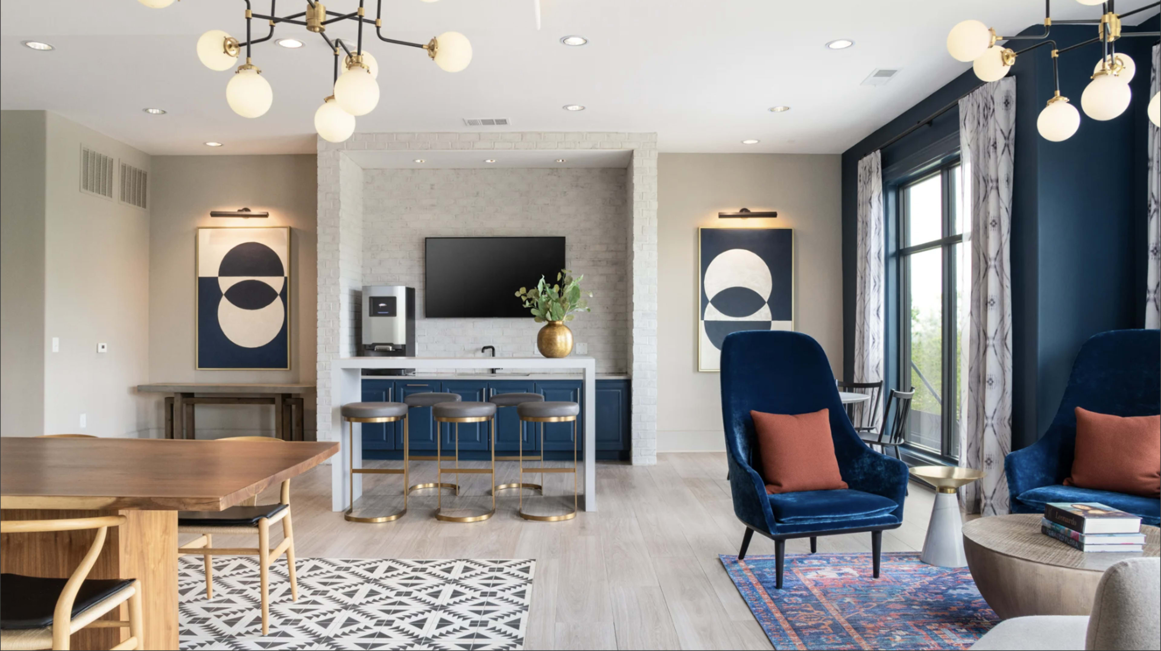 The image shows a modern living space with a dining area, a kitchen bar with stools, and a seating area featuring two blue chairs and decorative wall art.