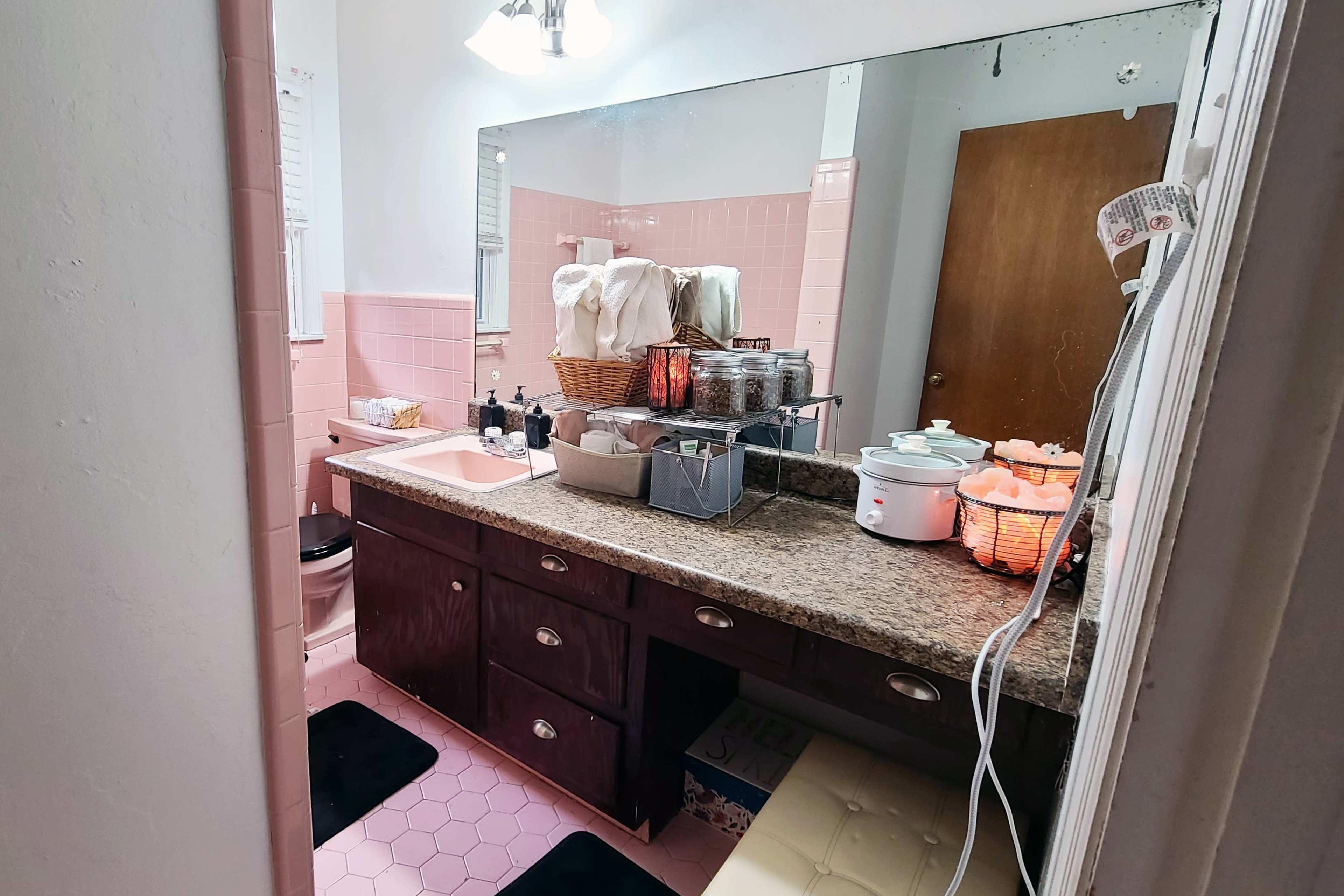 A pink-themed bathroom featuring a granite countertop, various toiletries, and an organized arrangement of baskets and containers on the sink.