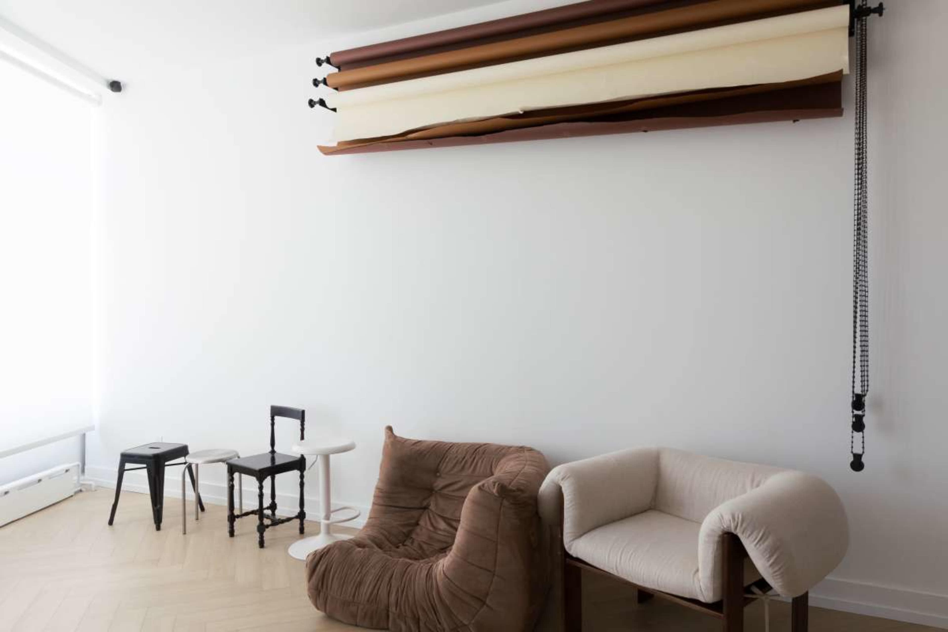The image features a minimalist room with two distinct chairs, a small round table, and a backdrop stand mounted on the wall above.