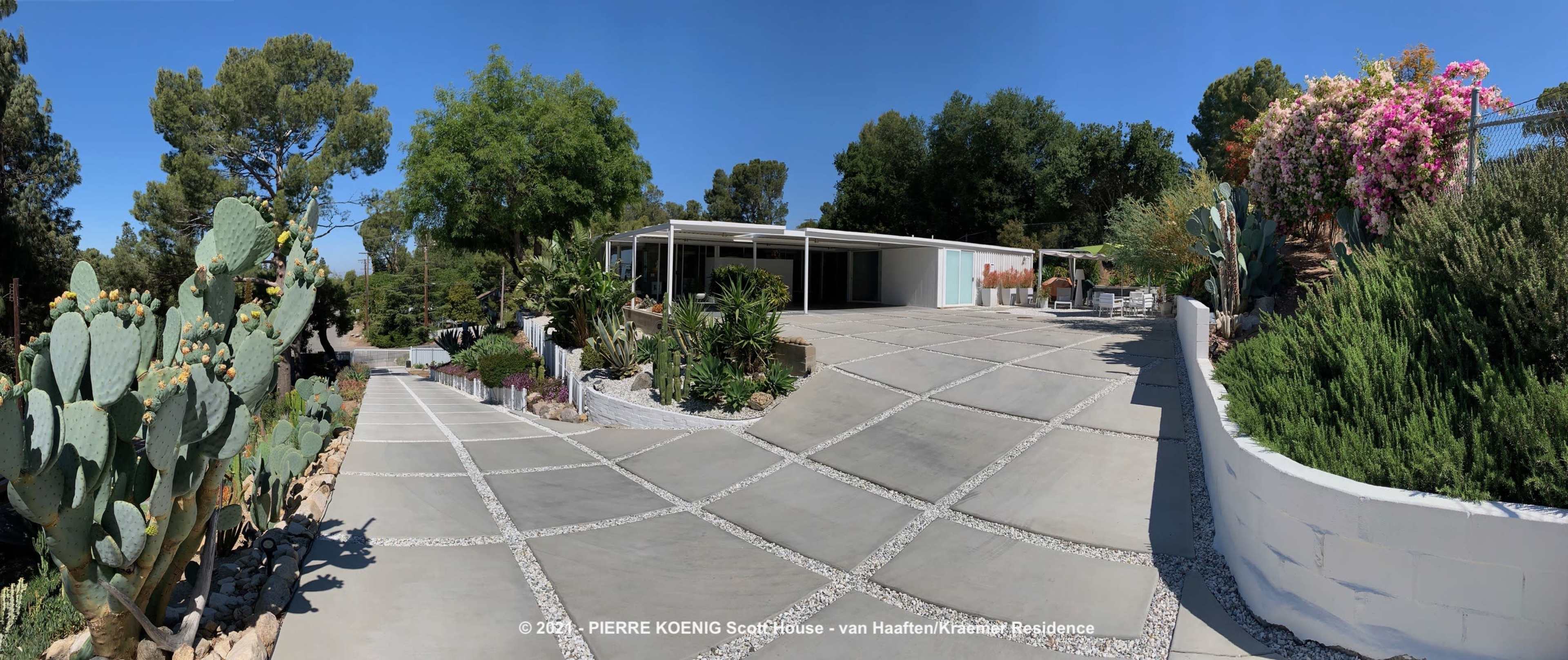 A modern single-story residence surrounded by landscaped greenery, pathways, and cacti.