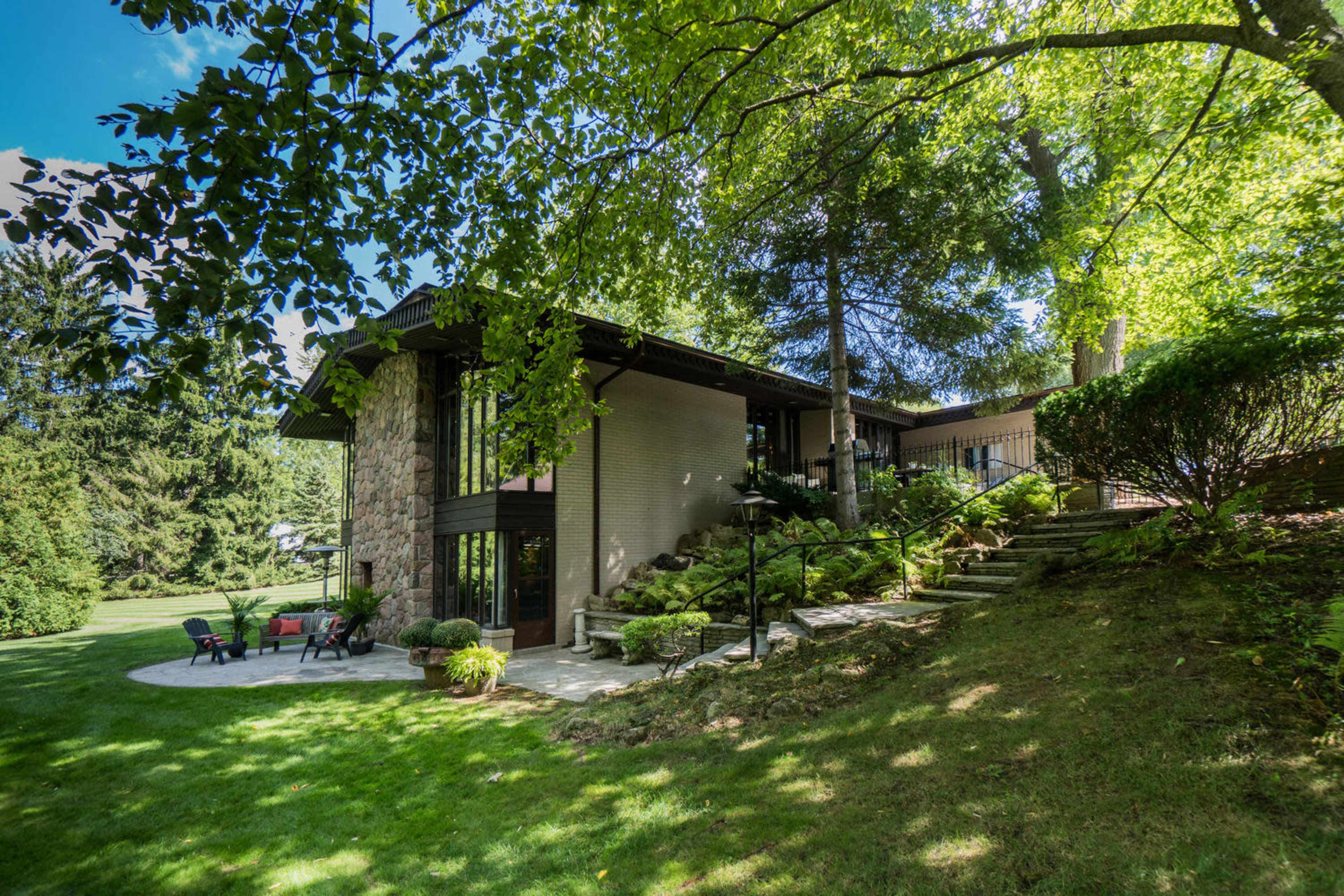 A modern house with a stone facade, surrounded by greenery and featuring a patio with seating.