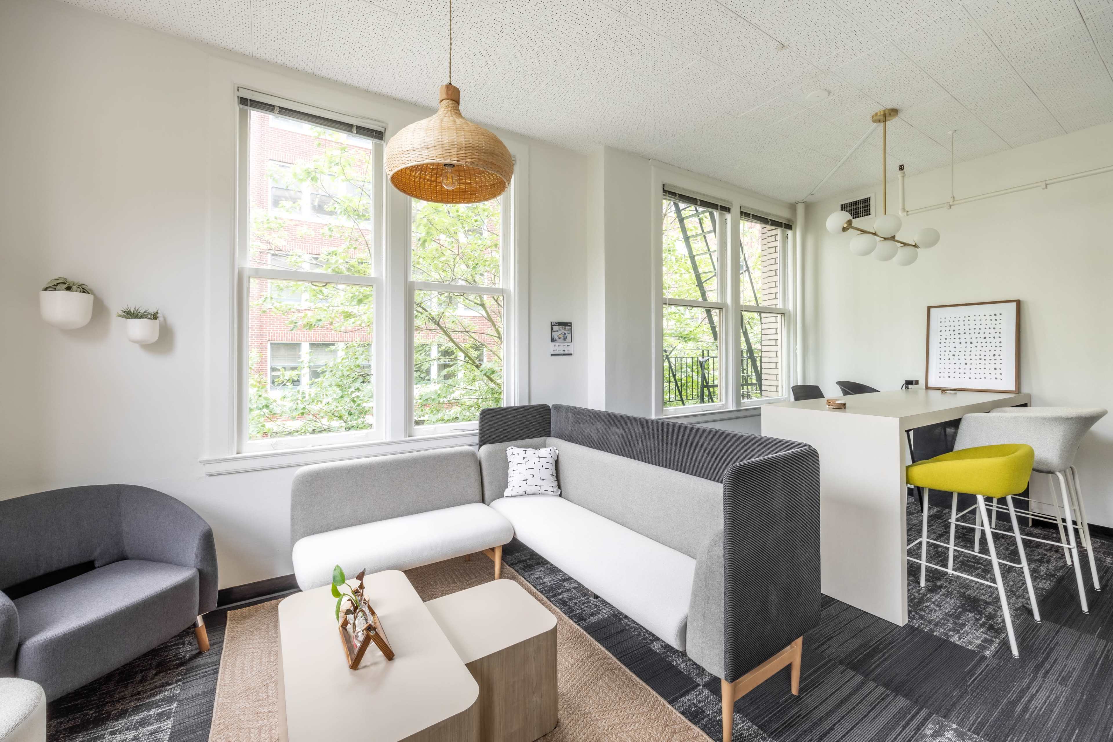 A modern lounge area with a gray and white sectional sofa, a light wood coffee table, and a dining space featuring high stools and a minimalist design.