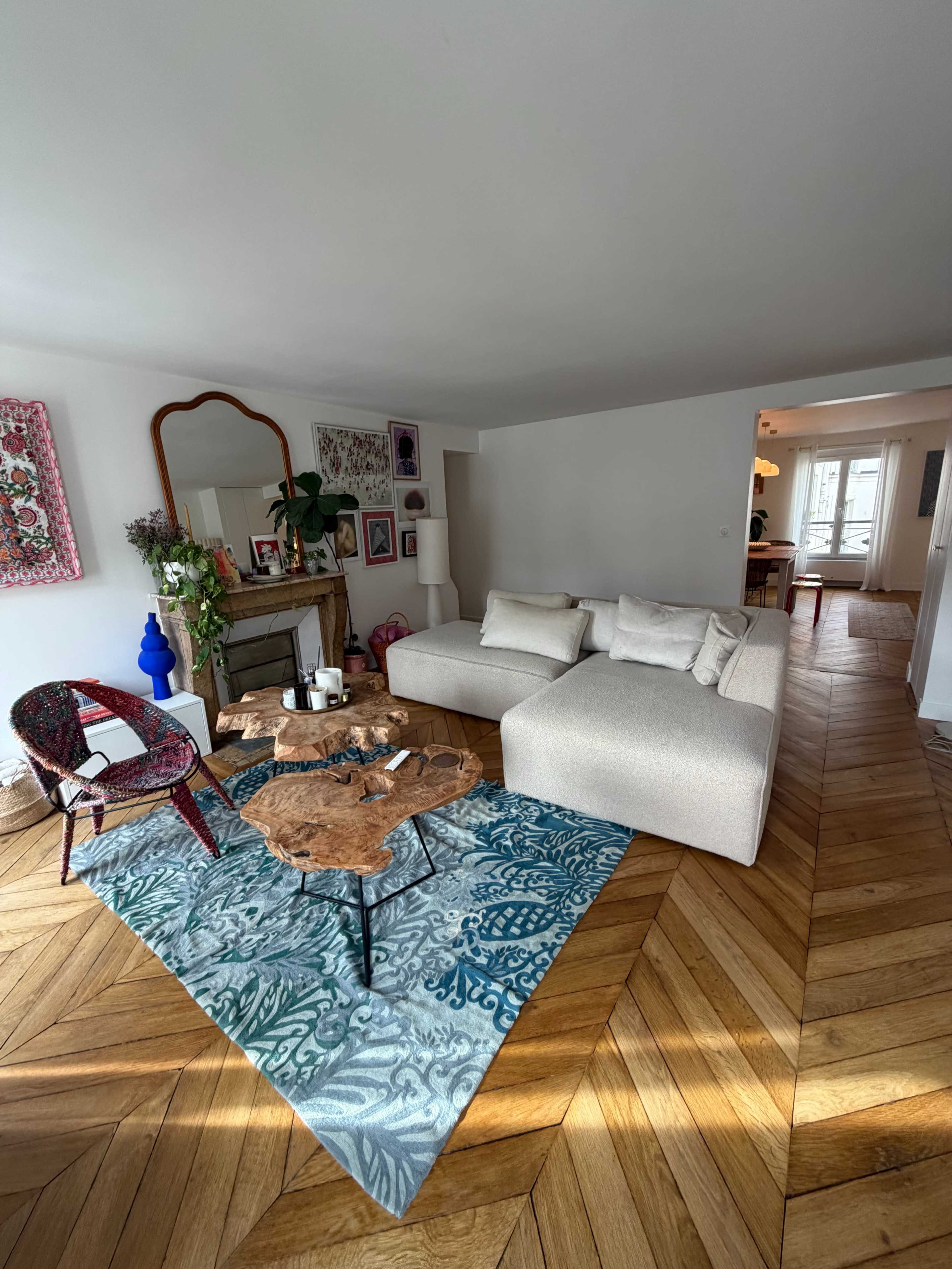 The image shows a modern living room with a plush sofa, a wooden coffee table, and an area rug, surrounded by decorative artwork and plants.