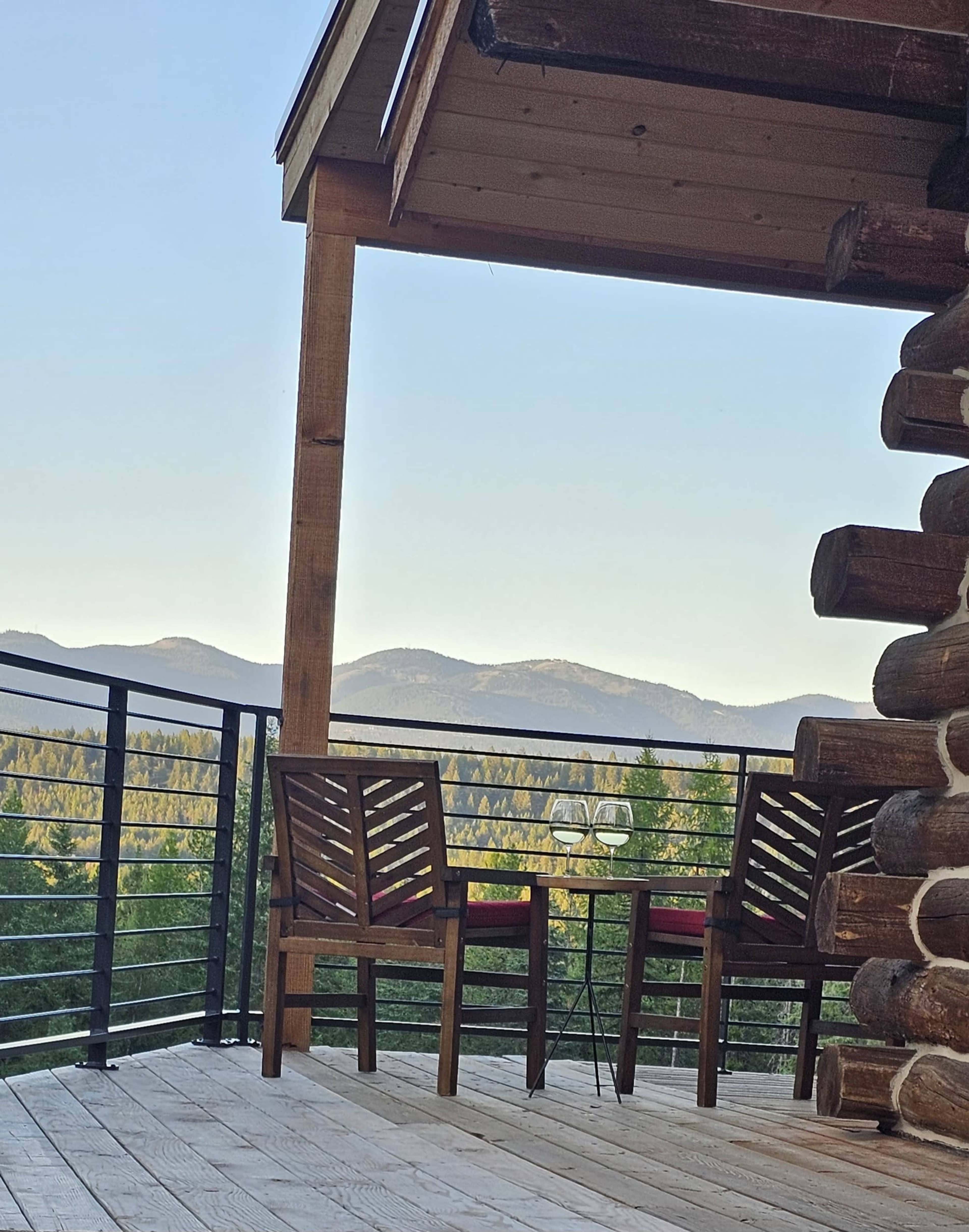 A wooden deck with two chairs and a table overlooks mountainous terrain in the distance.