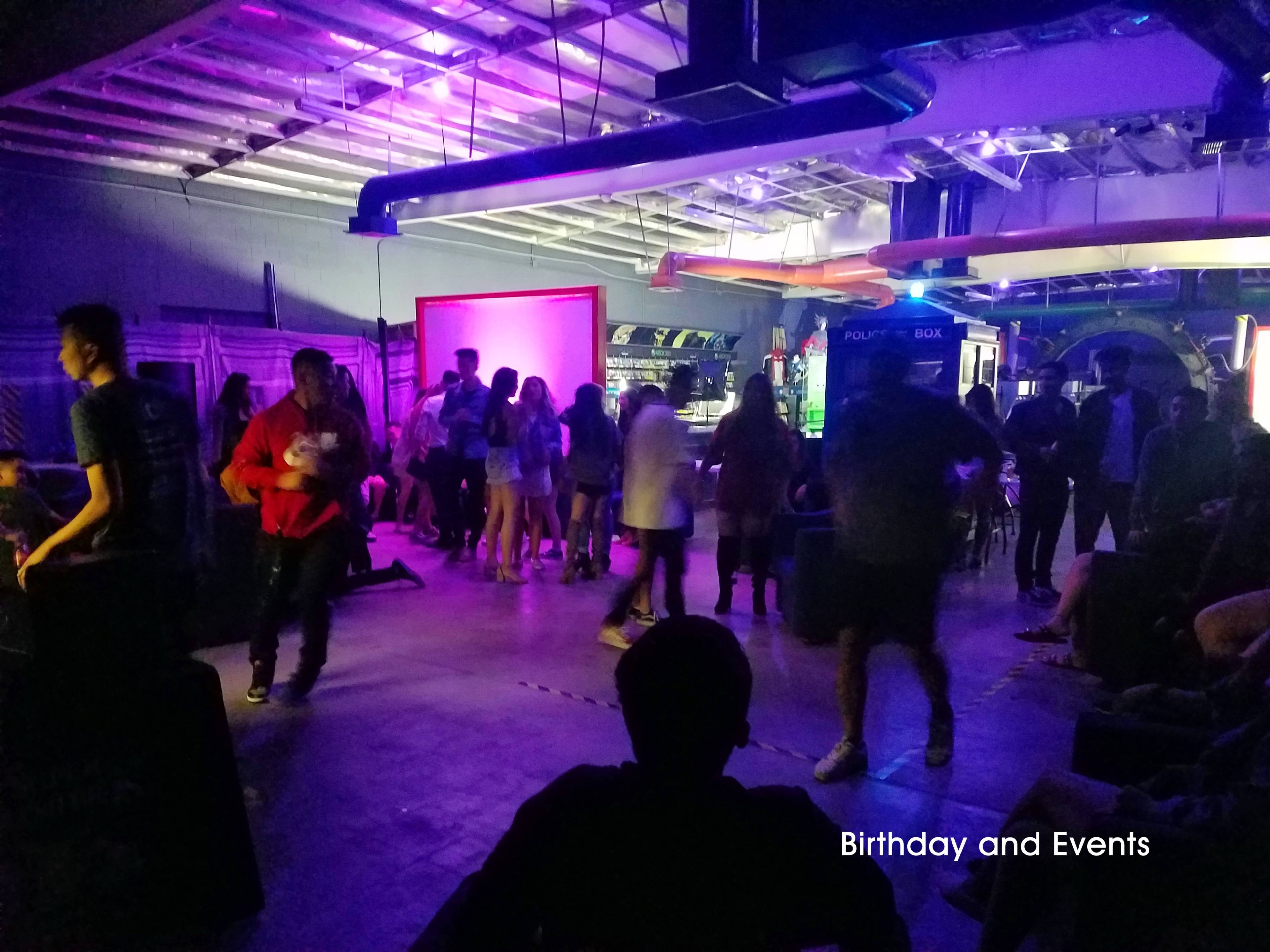 A crowd of people mingles and celebrates in a dimly lit venue with purple and blue lighting.