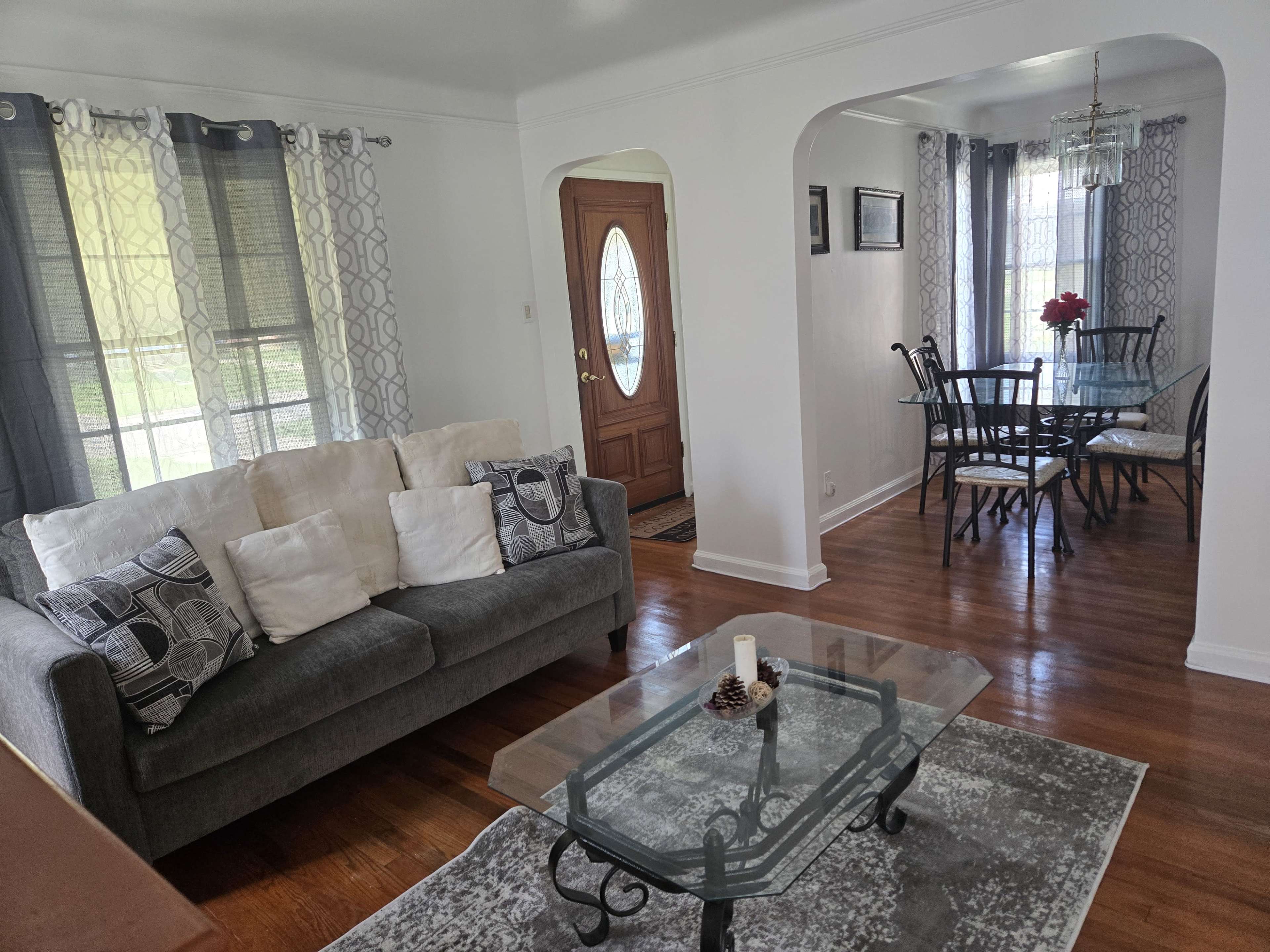 The image shows a living room with a gray sofa and coffee table, connecting to a dining area with a glass top table and chairs.