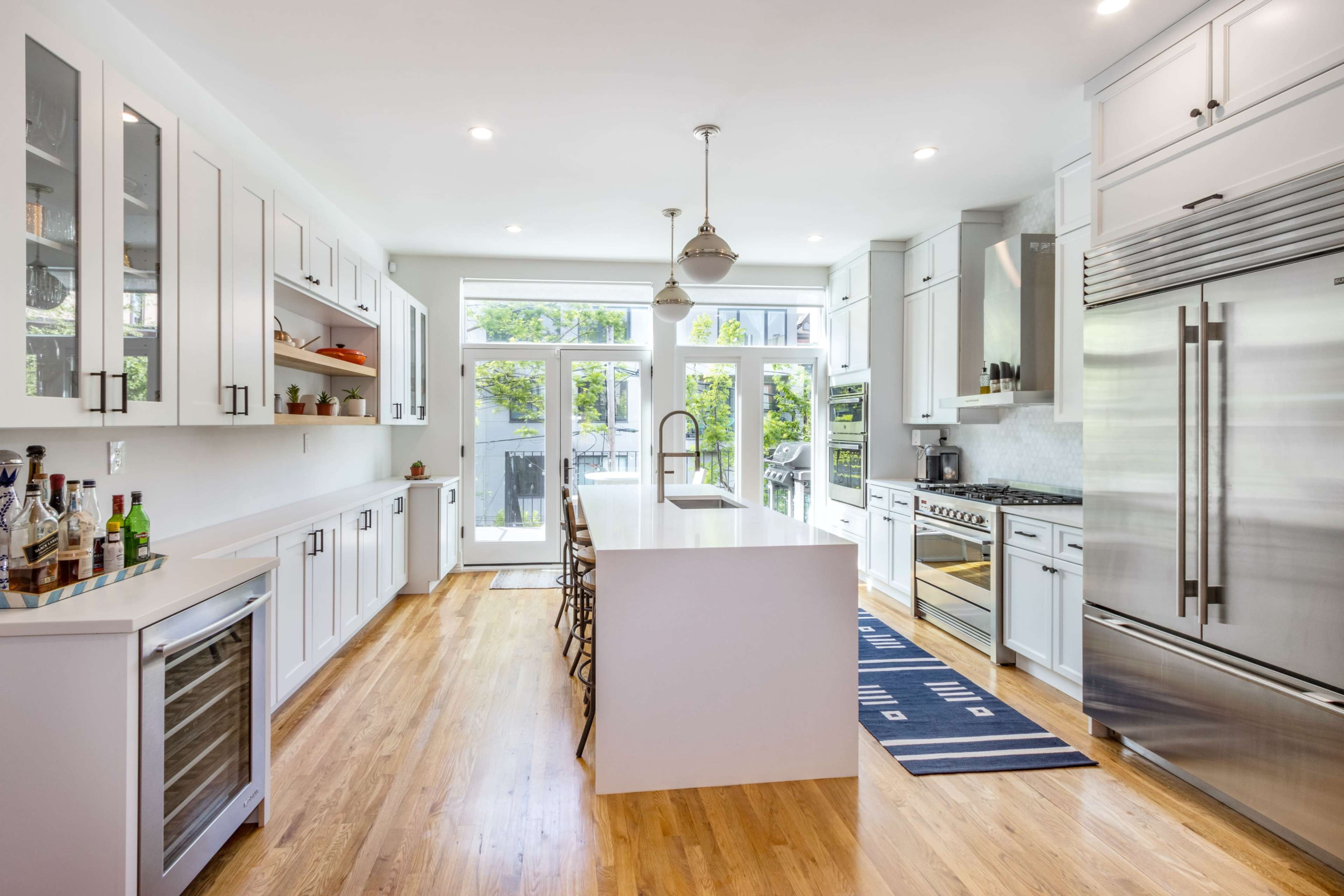 A modern kitchen features white cabinets, a large island with a sink, stainless steel appliances, and sliding glass doors leading to an outdoor space.