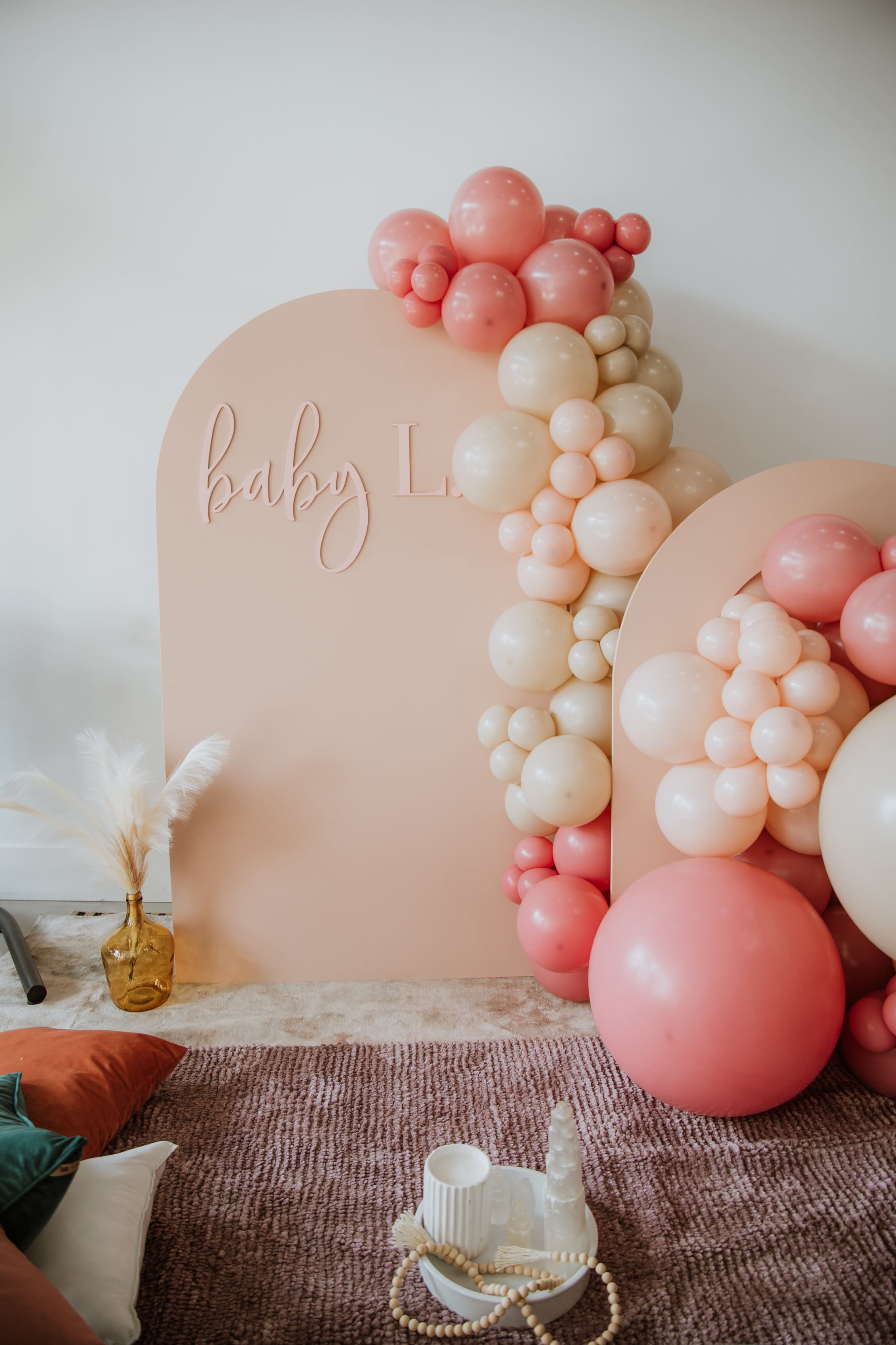 The image features a decorative display with large pastel-colored balloons arranged around a sign that reads "baby L," set against a neutral backdrop.