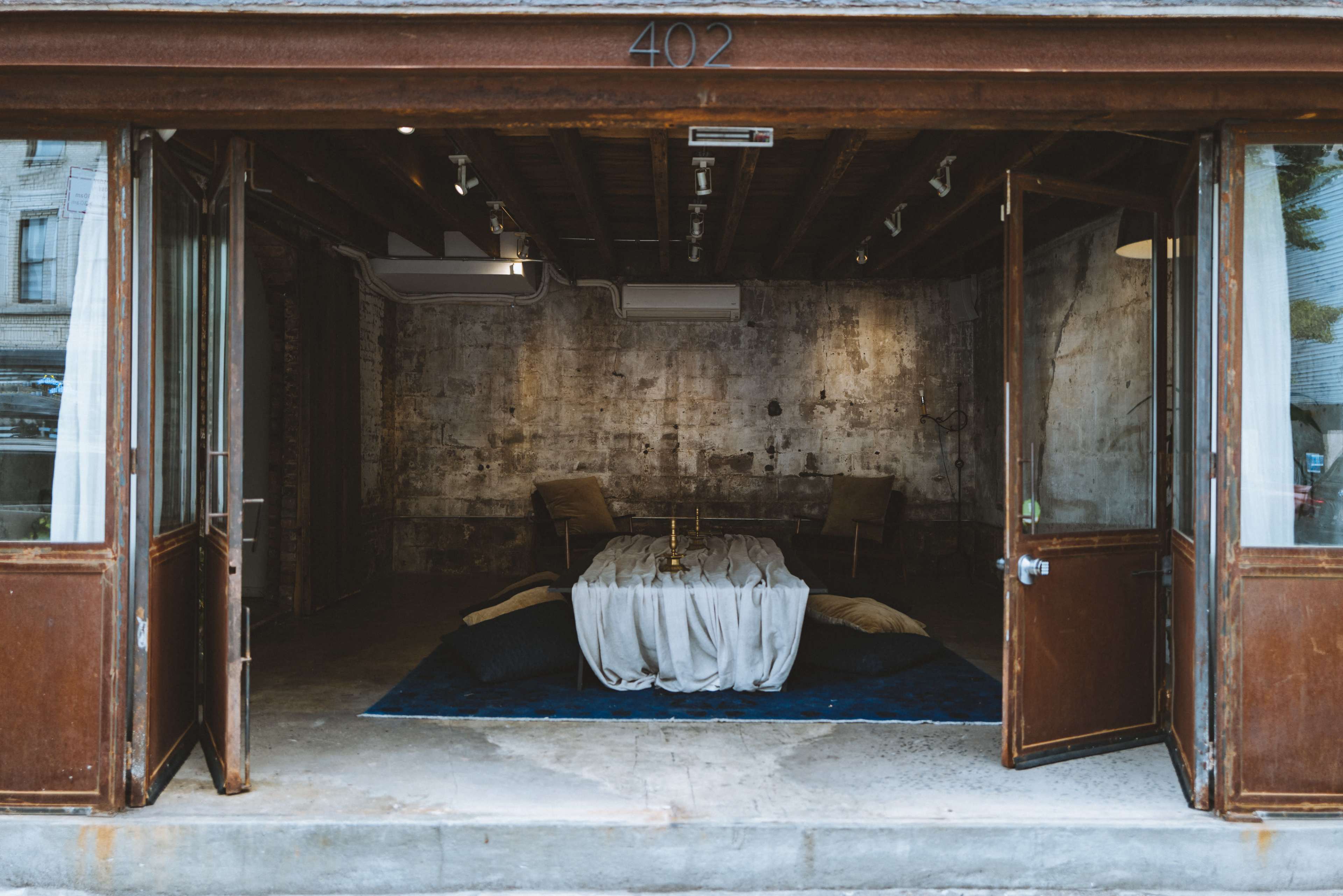 An open storefront with a rustic interior featuring a low table surrounded by cushions and two chairs.