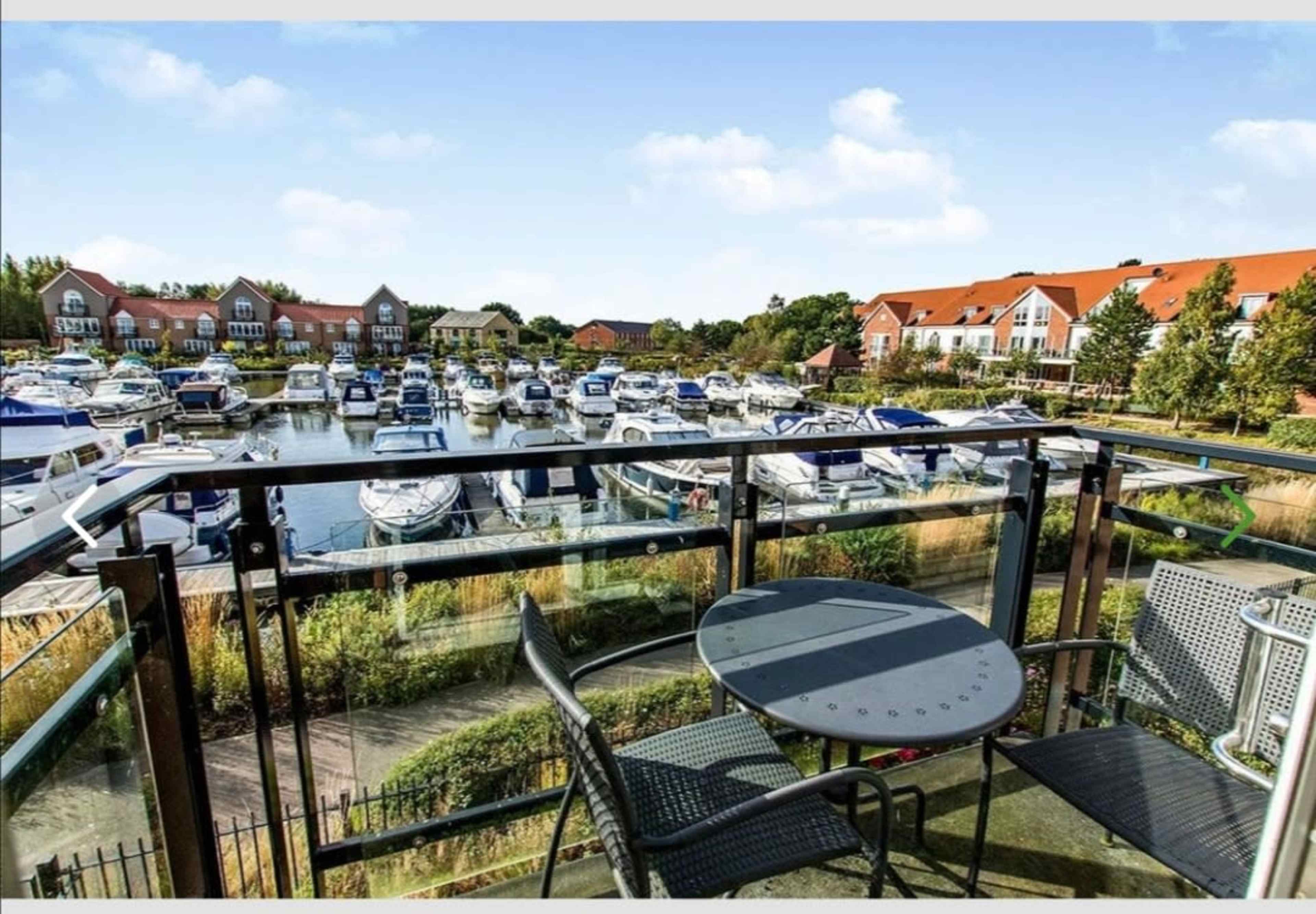 A balcony overlooks a marina filled with several boats, framed by residential buildings.