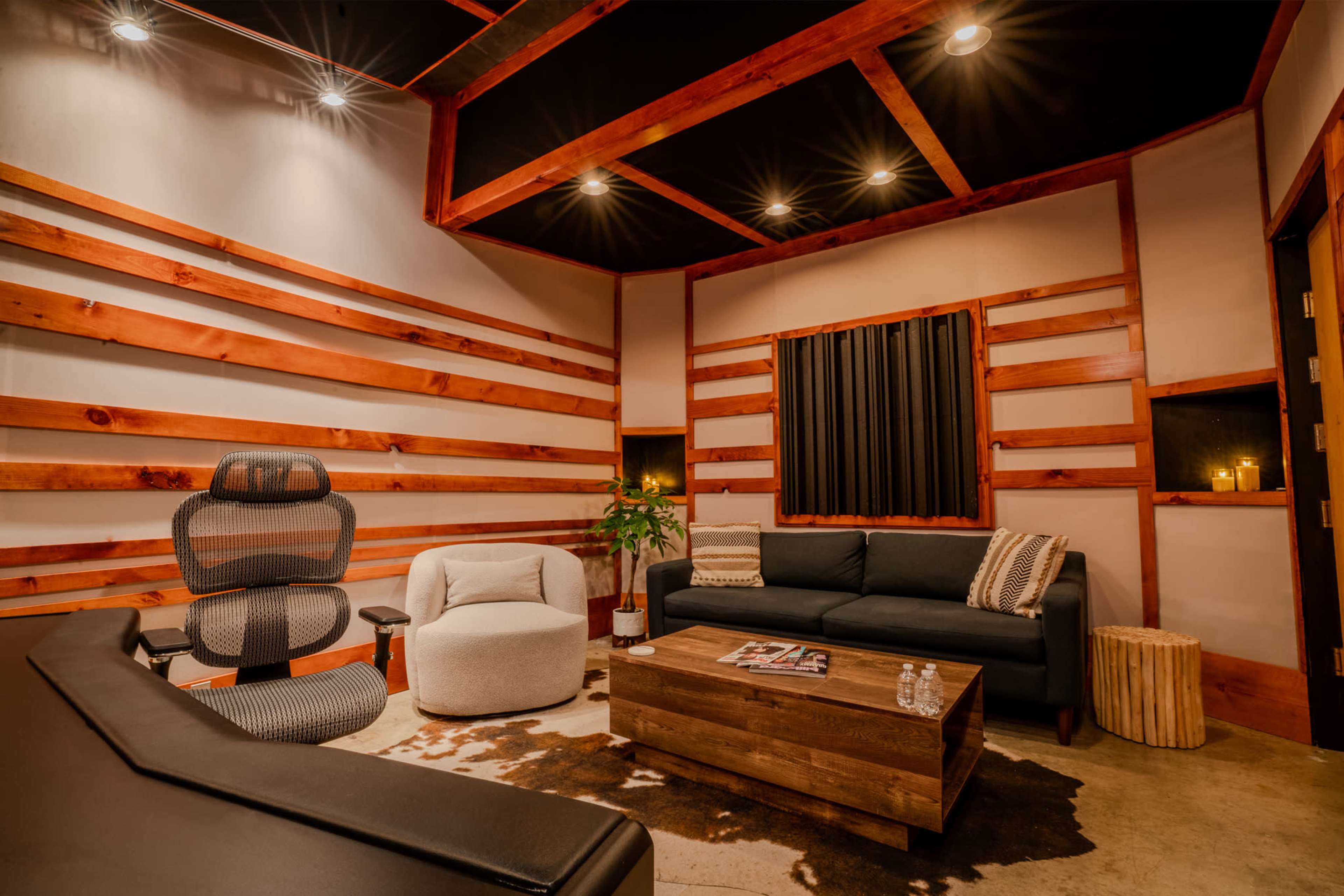 A modern lounge area with a dark couch, a round chair, a wooden coffee table, and wooden beam accents on the walls.