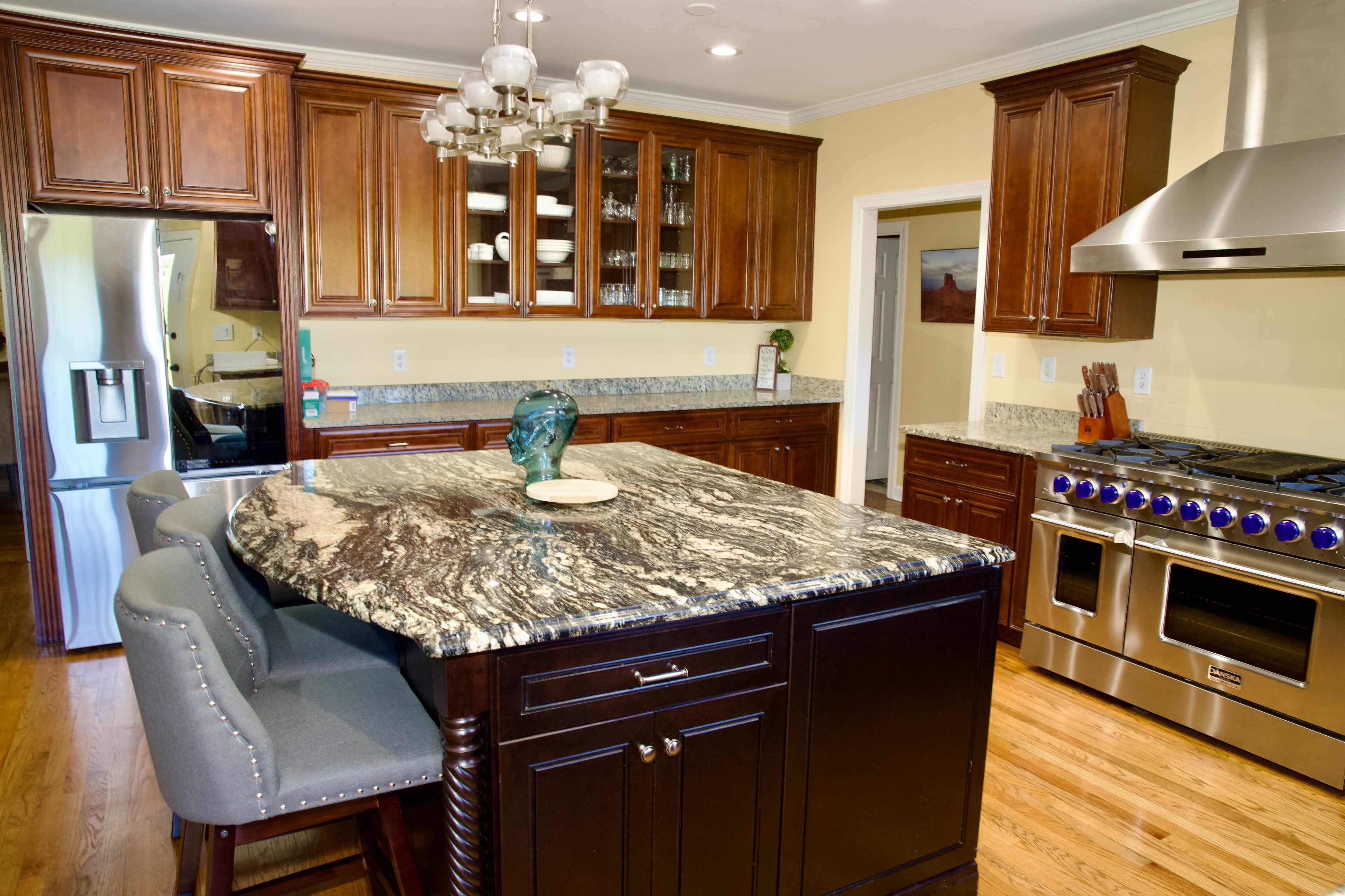 The kitchen features dark wooden cabinetry, a large granite countertop island with seating, and stainless steel appliances.
