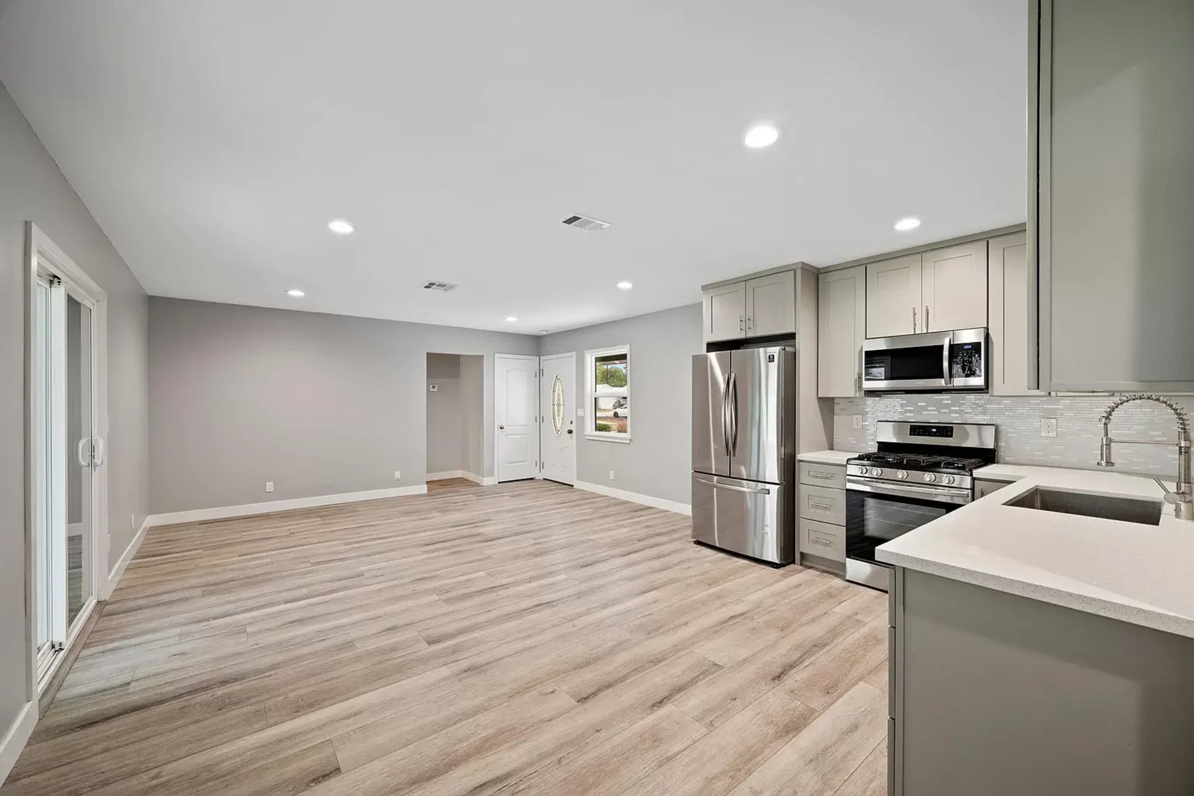 A modern kitchen and living area with grey walls, light wood flooring, and stainless steel appliances.