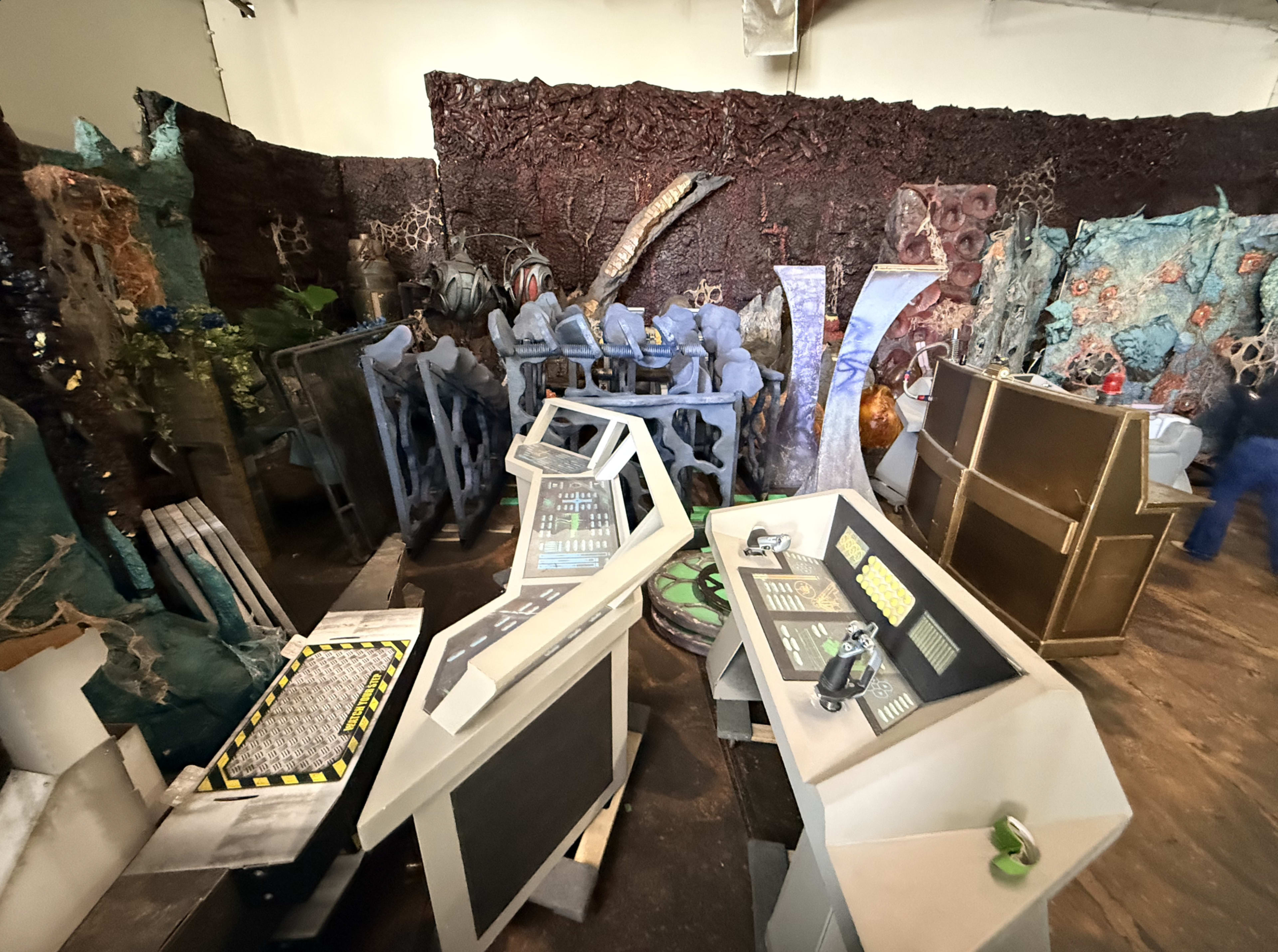 The image shows a fantastical room filled with elaborate sci-fi props, including control panels, unusual sculptures, and various colored textures resembling alien landscapes.