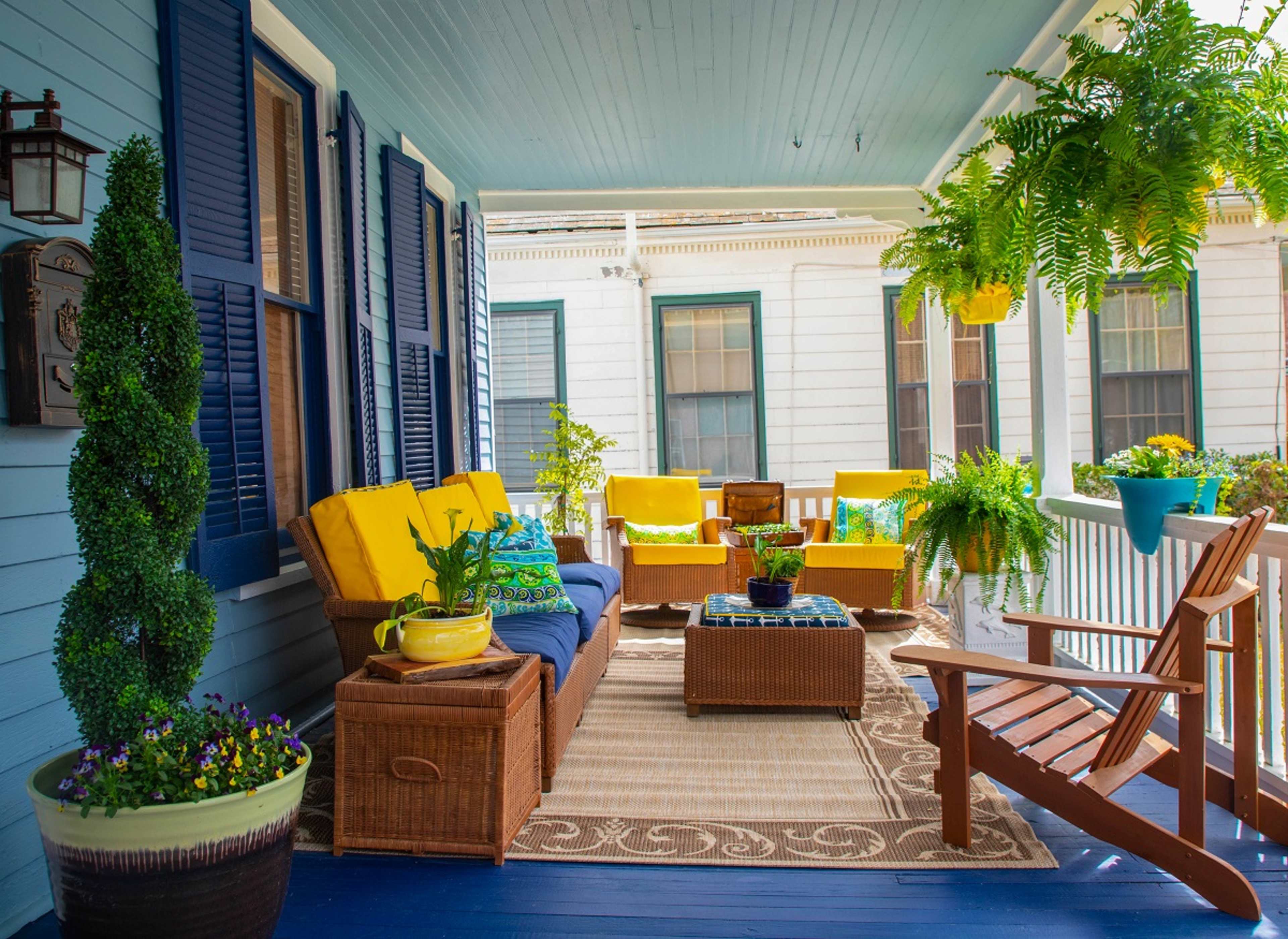 A porch decorated with yellow cushions, a brown wicker seating arrangement, and various houseplants.